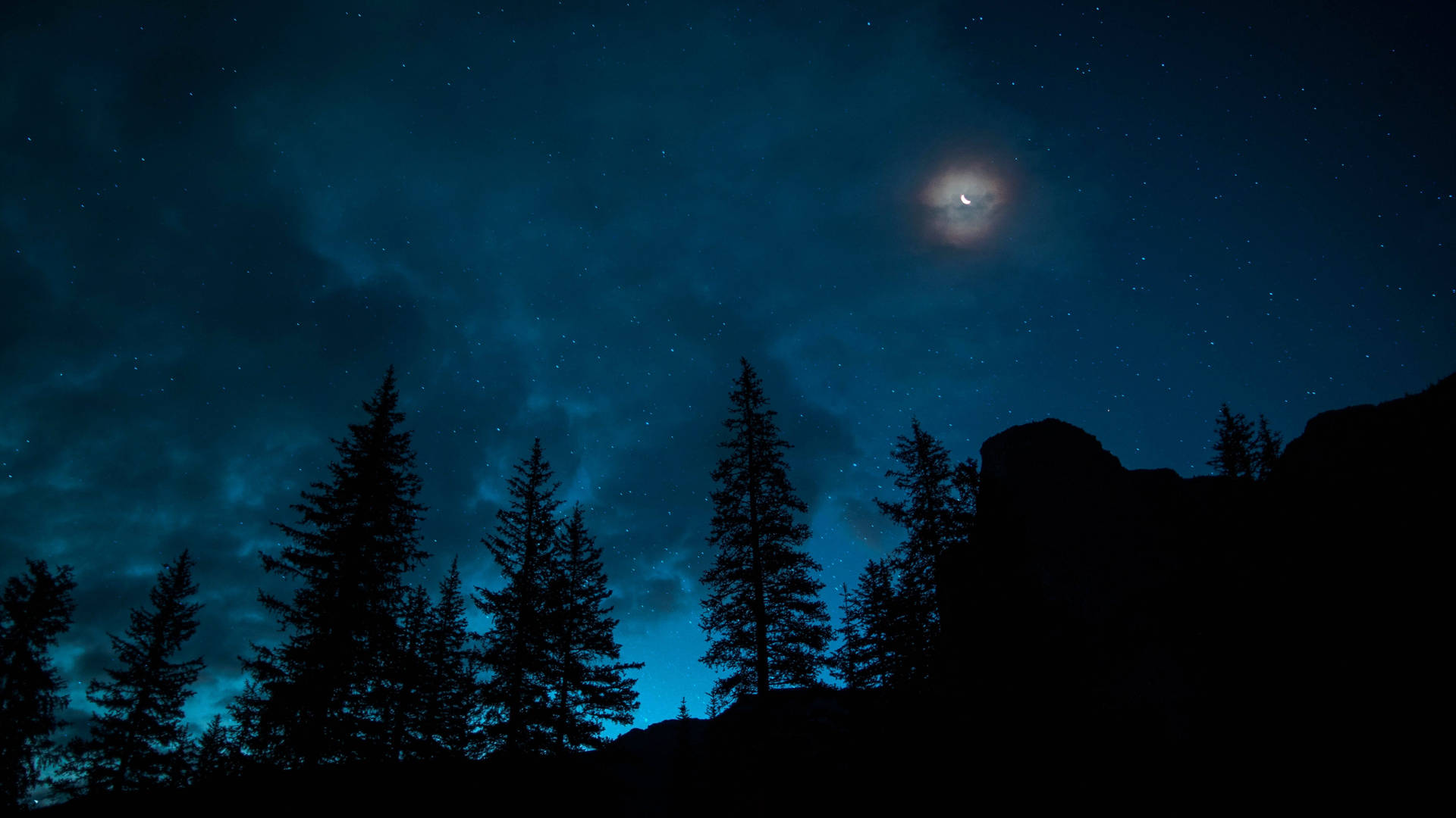 在繁星點點的夜空下，松樹和岩石的剪影，伴隨著發光的彎月。 — 3840x2160 動態圖片 壁紙