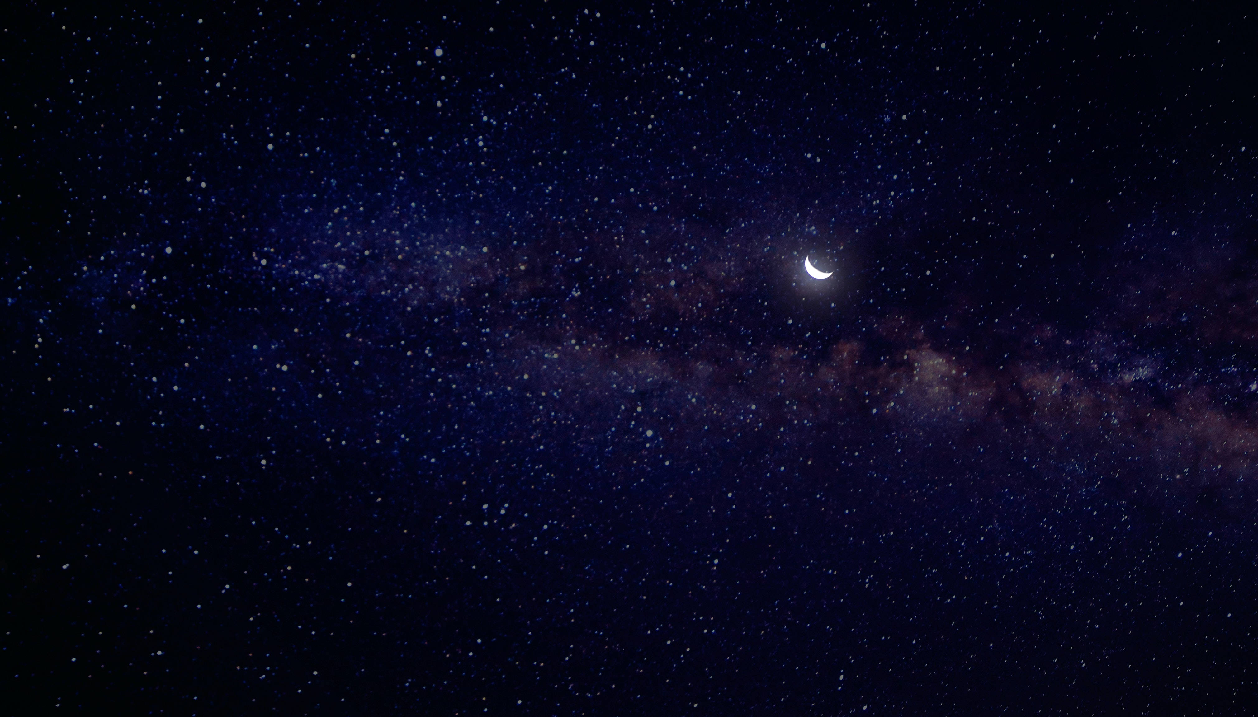 Crescent Moon 桌布 壁紙 — 一彎新月在銀河系的發光帶上方柔和地發光，映襯著深邃的星空夜空。