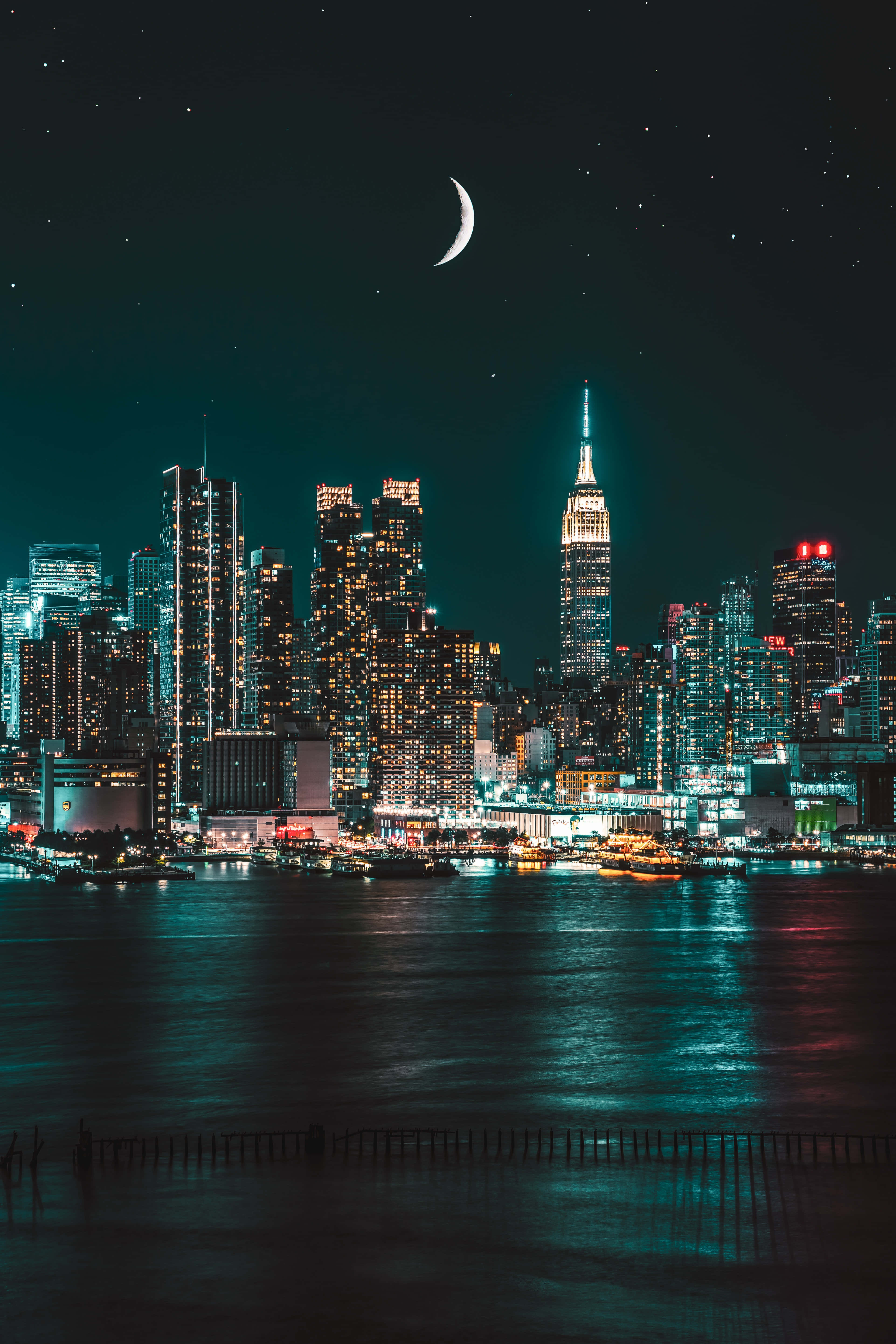 夜景城市 桌布 壁紙 — 一彎新月懸掛在閃爍的夜景城市上空，摩天大樓倒映在暗水中。