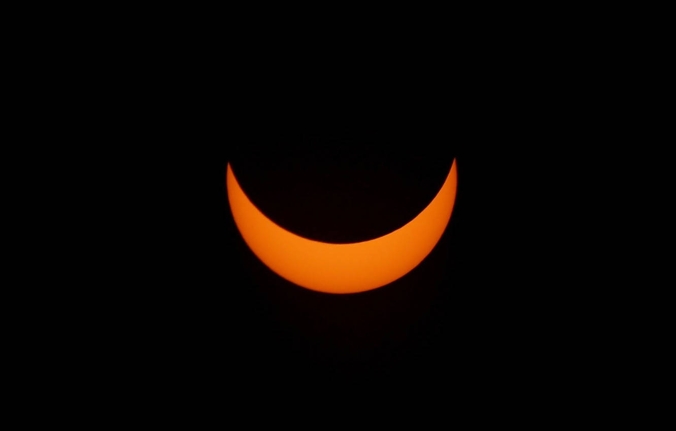 Eclipse 桌布 壁紙 — 一彎橙色太陽在日食期間，在漆黑的天空中隱約發光。