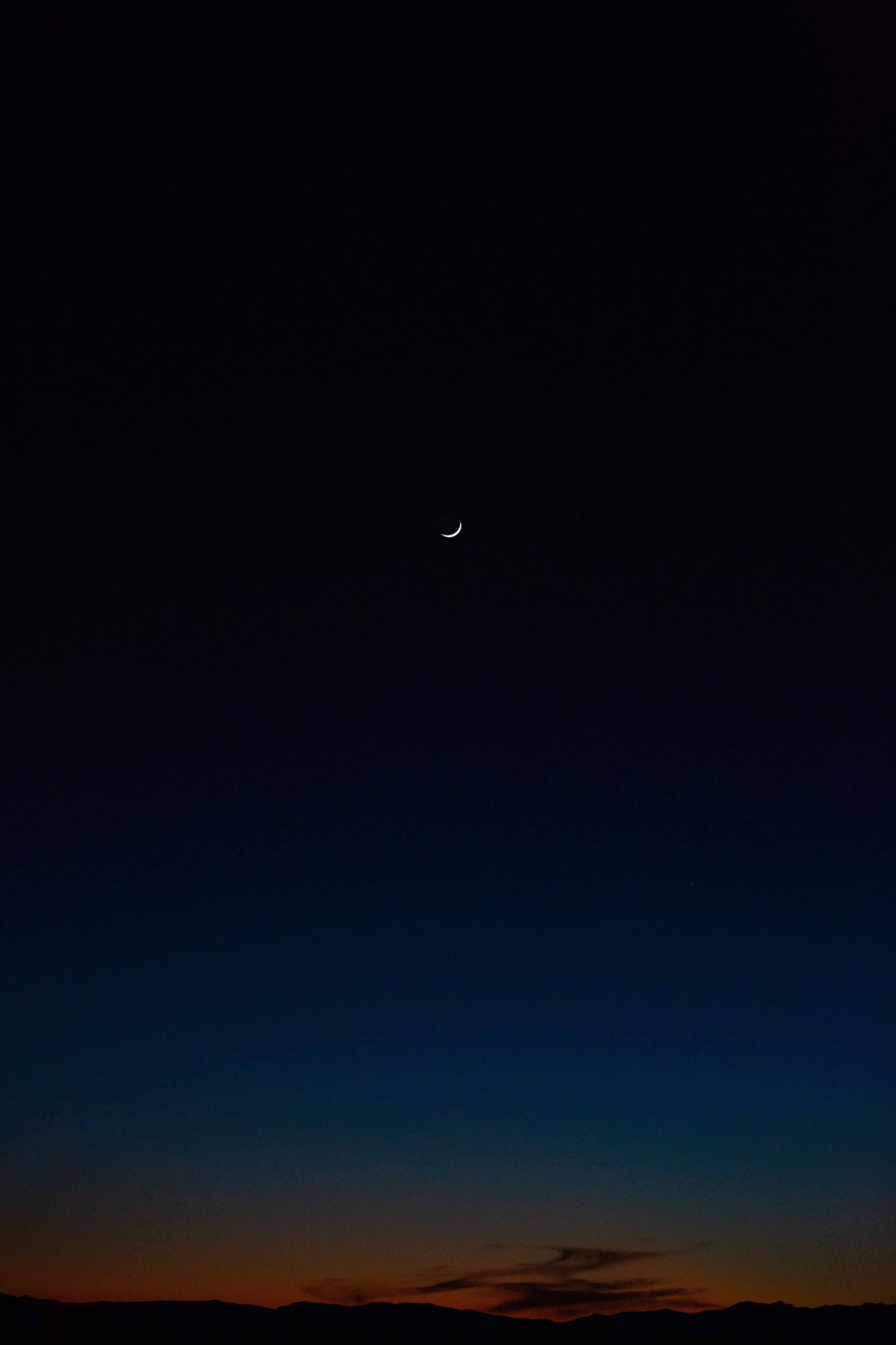 夜空 桌布 壁紙 — 一彎纖細的新月在深沉的暮色天空中閃耀，映襯著輪廓分明的山巒。