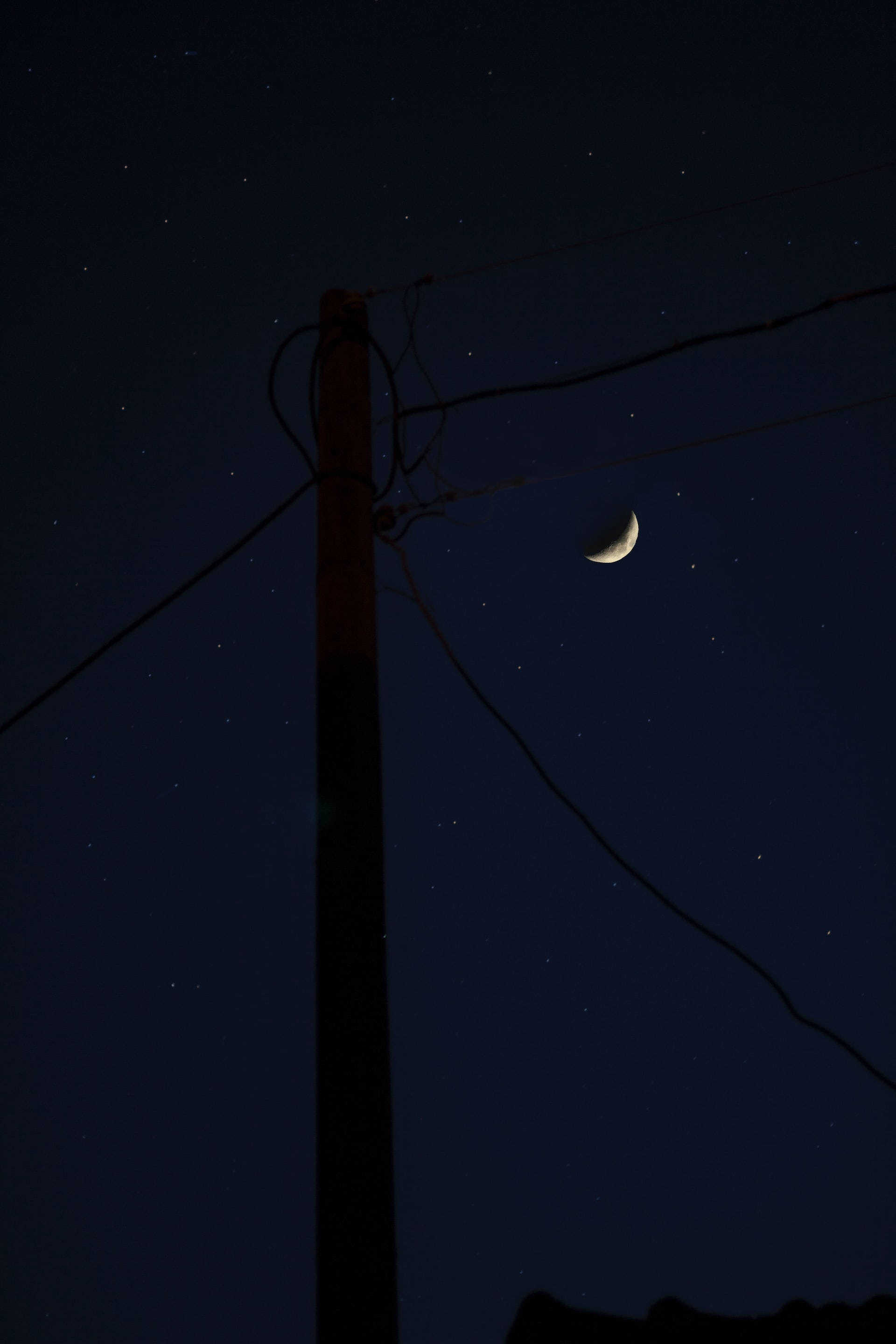 Crescent Moon 桌布 壁紙 — 一彎纖細的月牙在繁星點點的夜空下閃耀，背景是木製電線桿和電線的剪影。