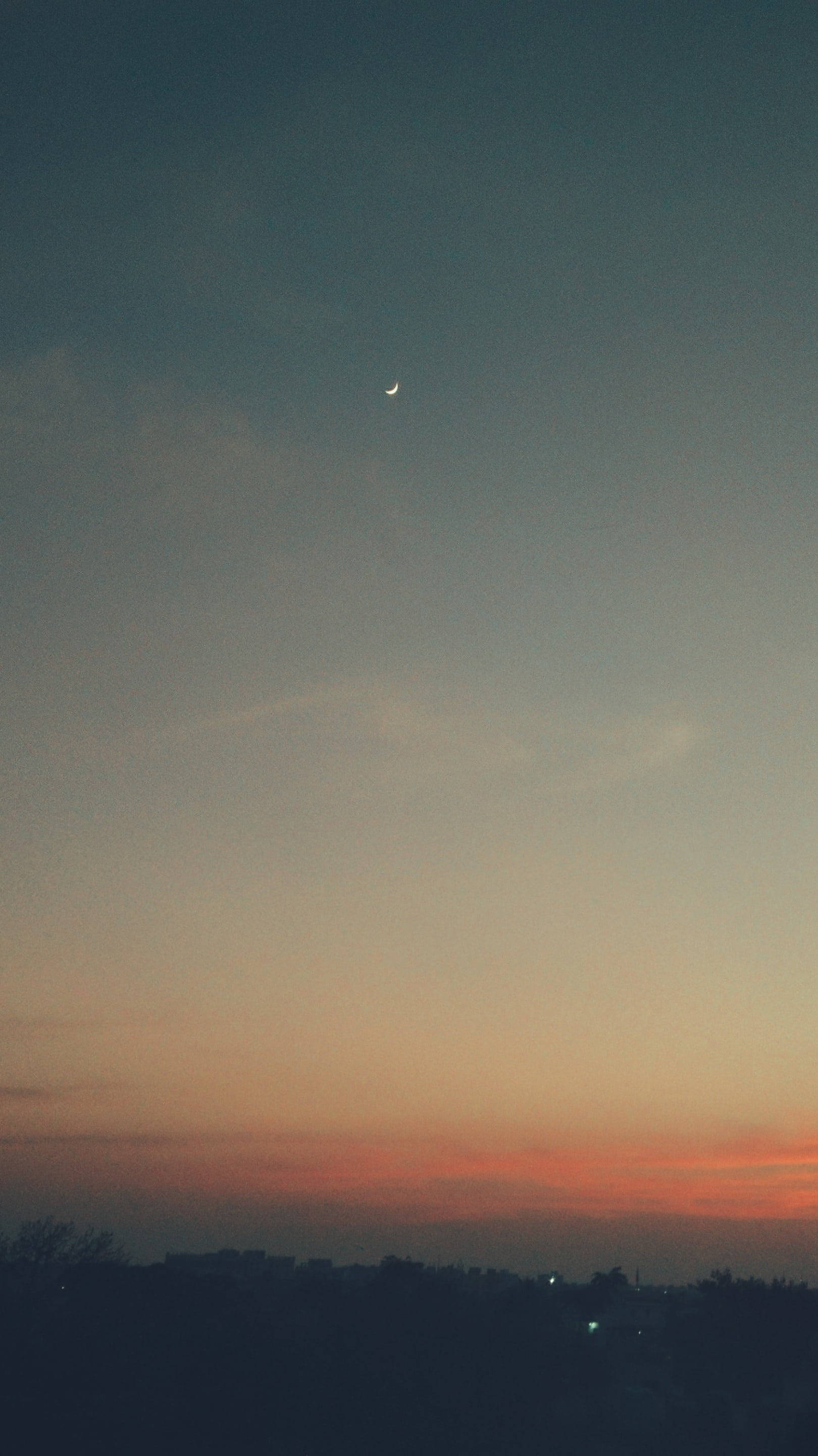 Aesthetic Sunset 桌布 壁紙 — 一彎纖細的月牙懸掛在暮色天空中，天空塗上柔和橙色和藍色調，下方是黑暗剪影的城市景觀。
