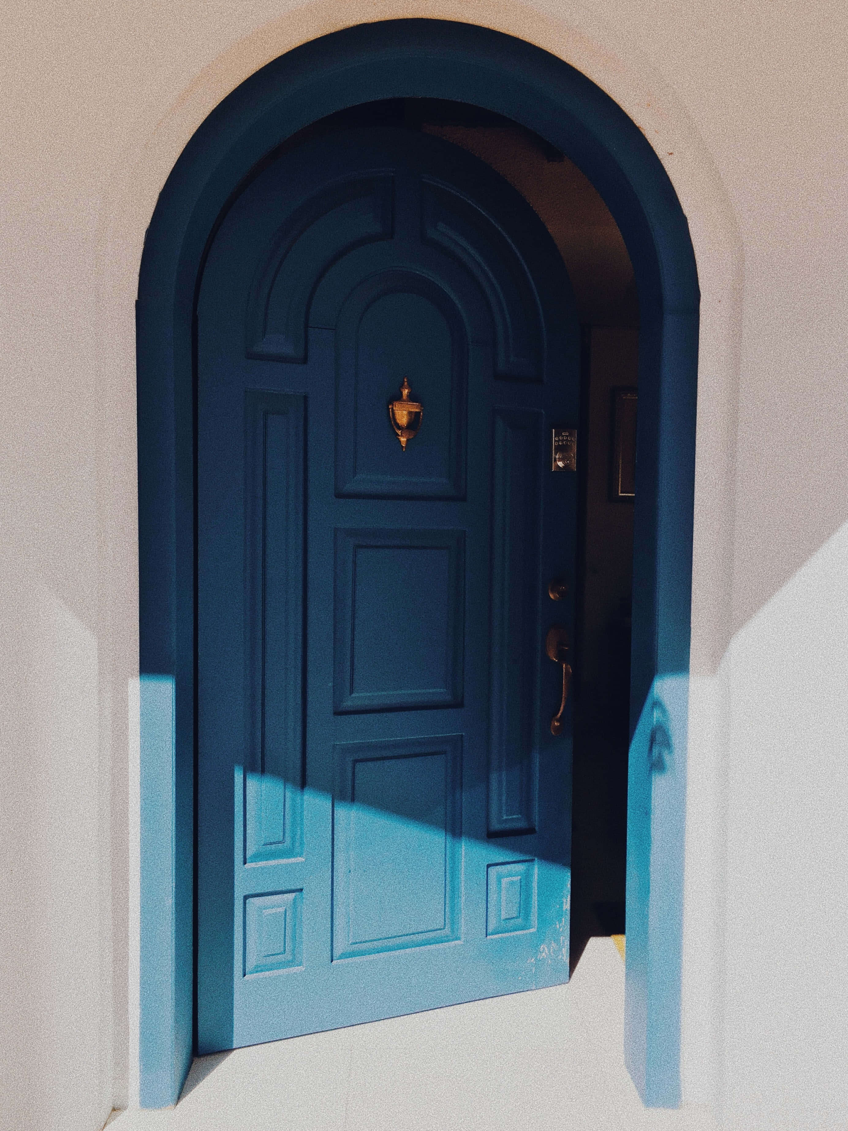 Door 桌布 壁紙 — 一扇充滿活力的藍色拱門，配以金色五金件，在明亮的陽光下，在白色灰泥牆上投下清晰的陰影。