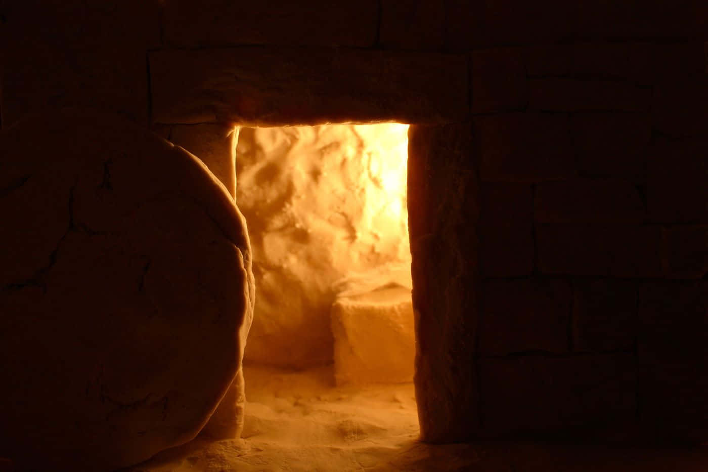 Empty Tomb 桌布 壁紙 — 一扇巨大的石門坐落於昏暗的石室中，門檻後透出溫暖的金色光芒。