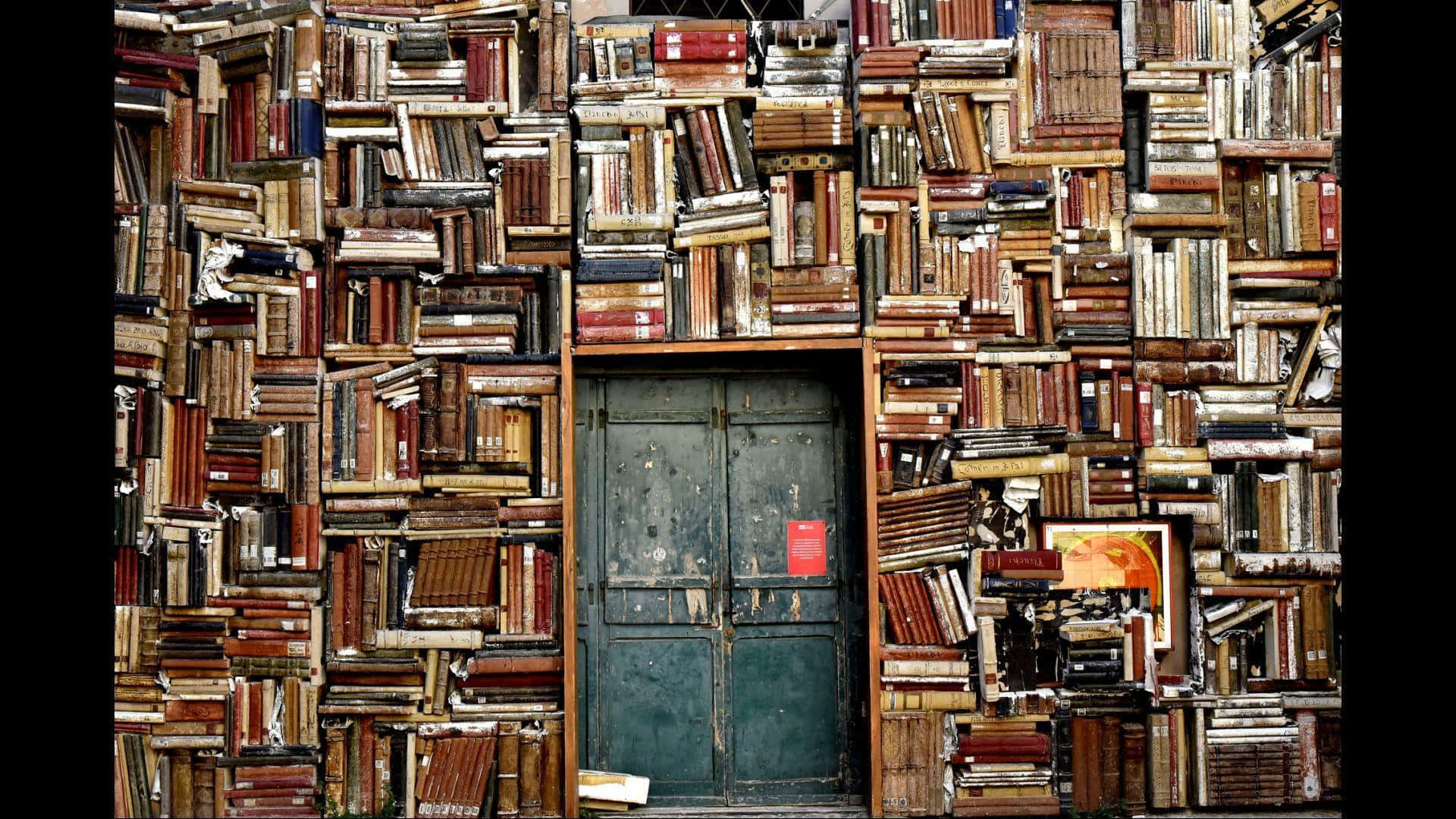 Library 桌布 壁紙 — 一扇風化的綠色門，被密集混亂的堆疊復古書籍牆所環繞，書籍呈溫暖的棕色和褪色的紅色。