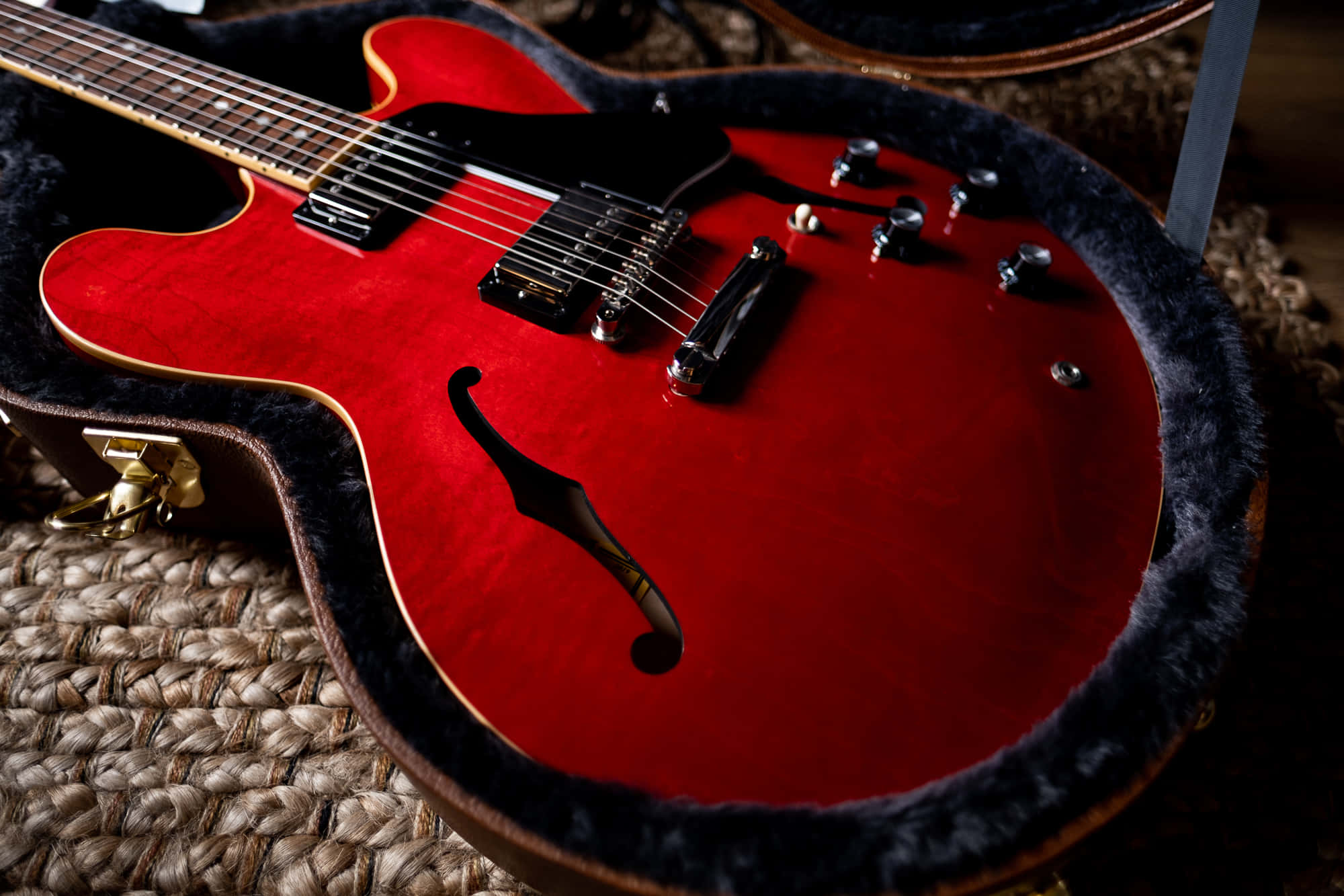 Guitar Aesthetic 桌布 壁紙 — 一把亮面紅色電吉他放在打開的吉他盒內，置於編織地毯上，展示其f孔和鍍鉻硬件。