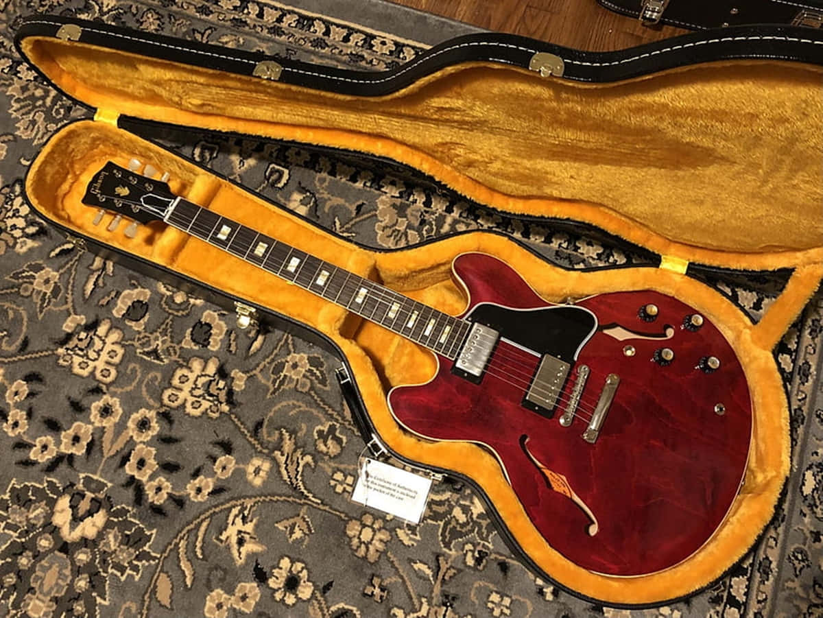Guitar Aesthetic 桌布 壁紙 — 一把亮面紅色電吉他放在打開的黃色內裡吉他盒內，置於圖案地毯上。