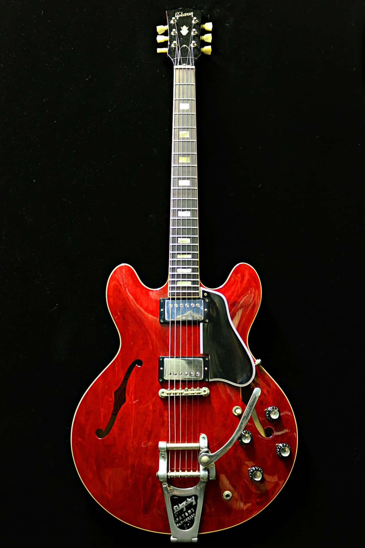 Guitar Aesthetic 桌布 壁紙 — 一把光澤的紅色 Gibson ES-335 電吉他，配有銀色配件，垂直立在純黑背景前。