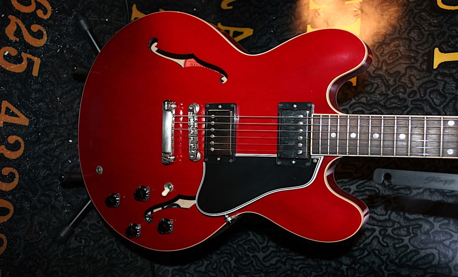 Guitar Aesthetic 桌布 壁紙 — 一把光澤的紅色半空心電吉他放在深色圖案表面上，溫暖的燈光突顯其曲線和硬體。