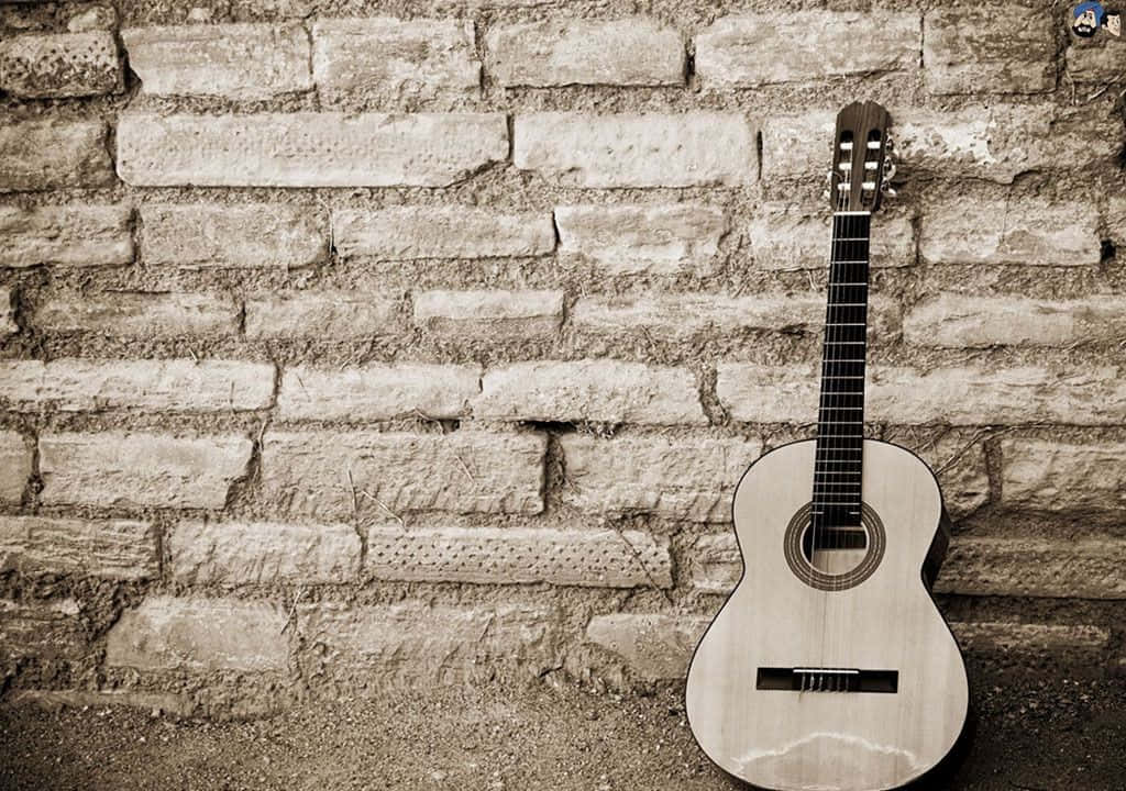 Musical 桌布 壁紙 — 一把古典吉他靠在一面風化的石牆上，呈現懷舊的褐色調構圖。