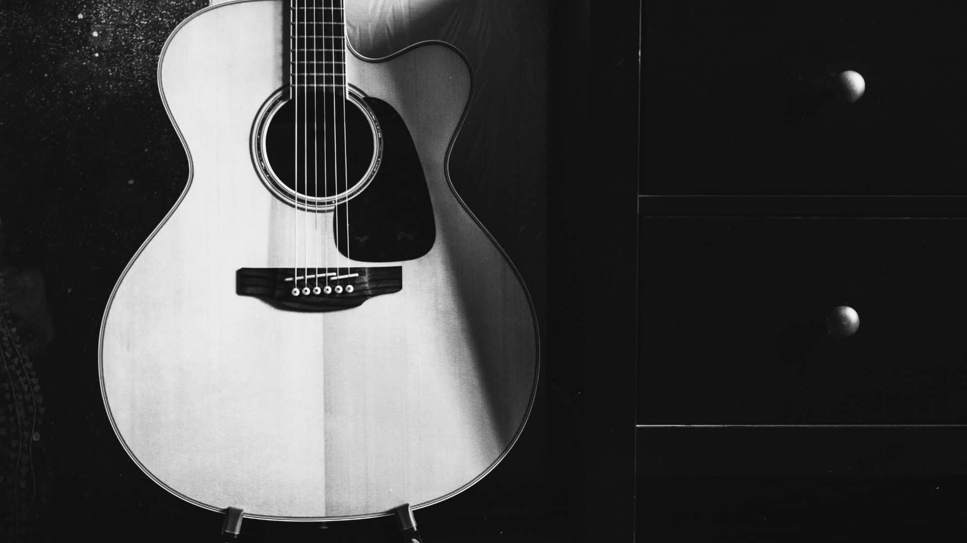 Black And White Guitar 桌布 壁紙 — 一把單色原聲吉他靠在一個帶有圓形把手的深色抽屜櫃上，處於簡約工作室環境。