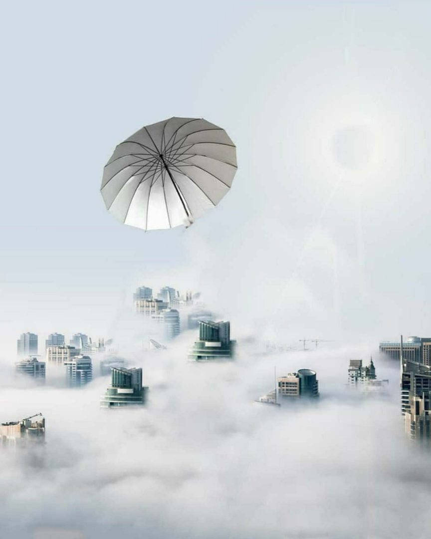 Vijay Mahar 桌布 壁紙 — 一把巨大的銀色雨傘在蒼白的天空下，靜靜地漂浮在部分被厚雲遮蓋的城市景觀之上。