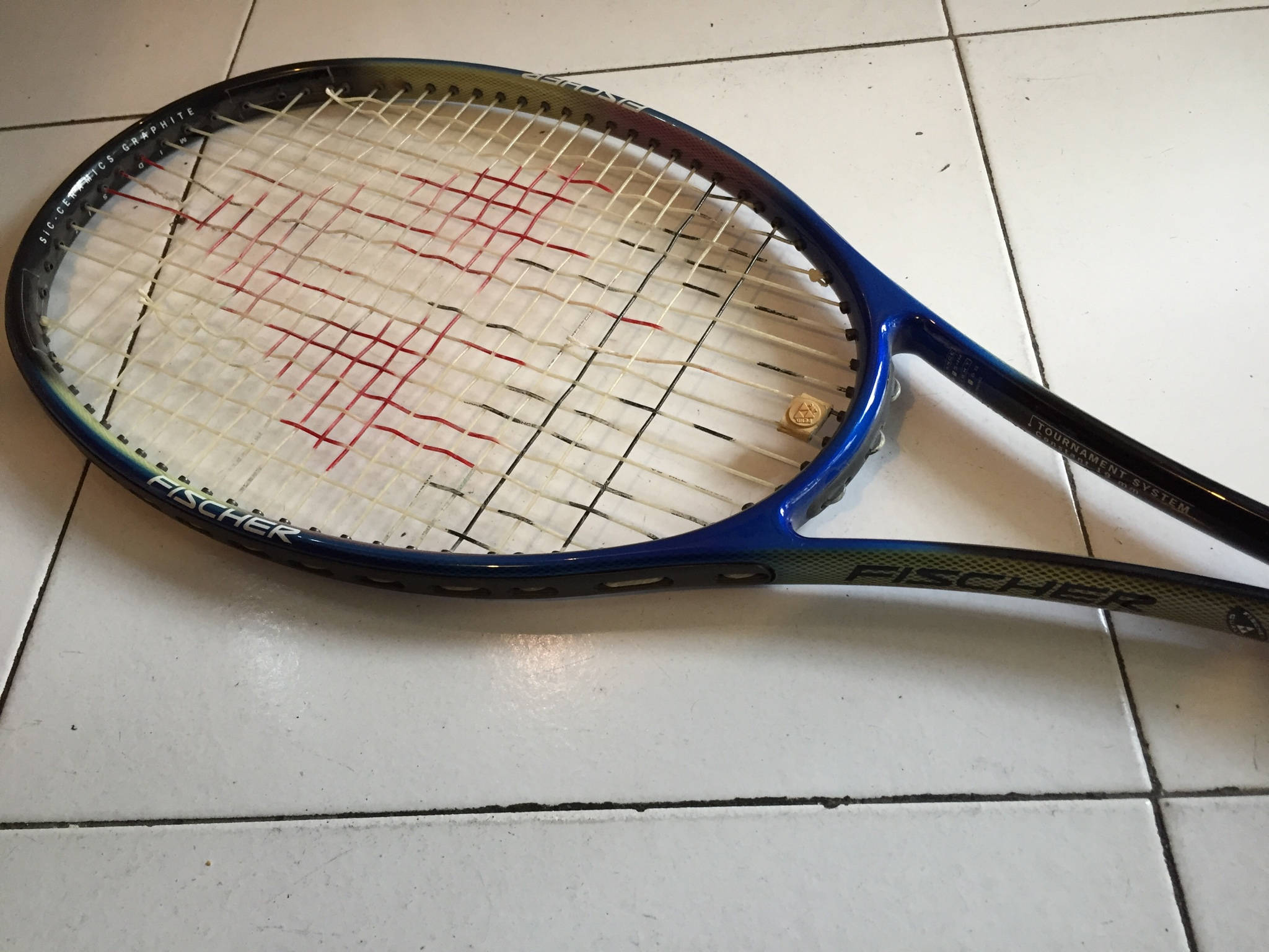 Champion 桌布 壁紙 — 一把帶有紅色線條標記的Fischer網球拍放在白色瓷磚地板上。