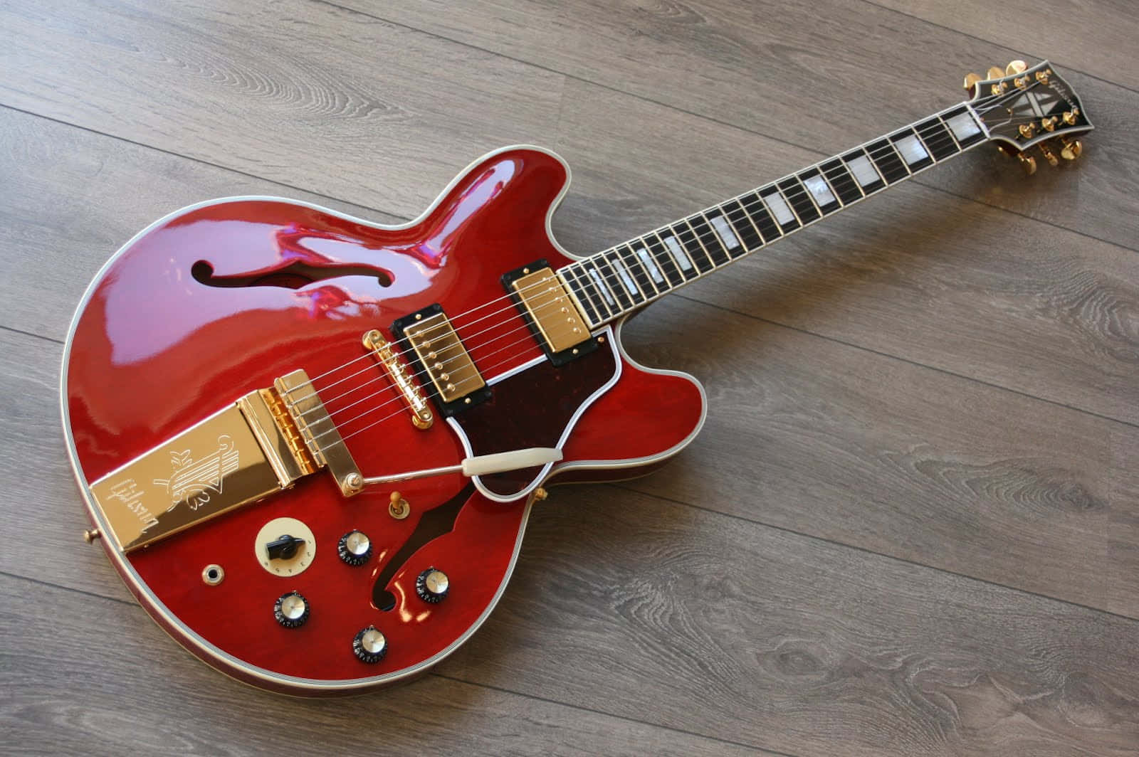 Guitar Aesthetic 桌布 壁紙 — 一把帶有金色硬體的亮紅色電吉他斜放在灰色木地板上。