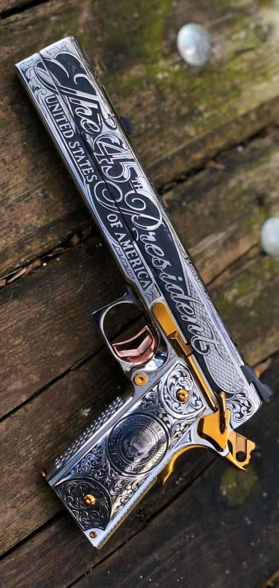 pistol 桌布 壁紙 — 一把帶有金色裝飾的華麗雕刻手槍放在風化的木板上，展示複雜的總統主題設計。