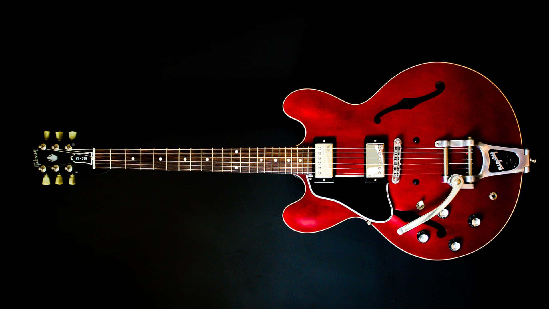 Guitar Aesthetic 桌布 壁紙 — 一把帶有銀色金屬配件的亮面紅色半空心電吉他，斜靠在純黑背景上。