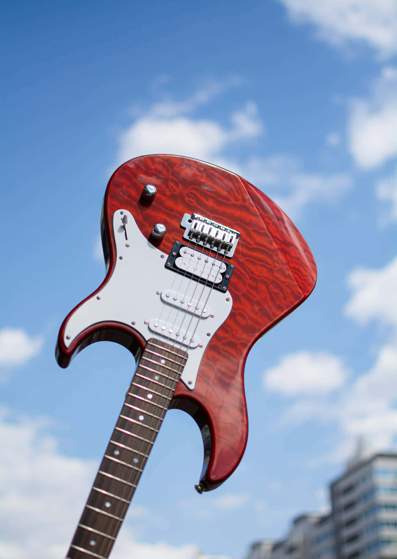 Guitar Aesthetic 桌布 壁紙 — 一把帶白色護板的亮紅色電吉他，在藍天白雲下高高聳立。