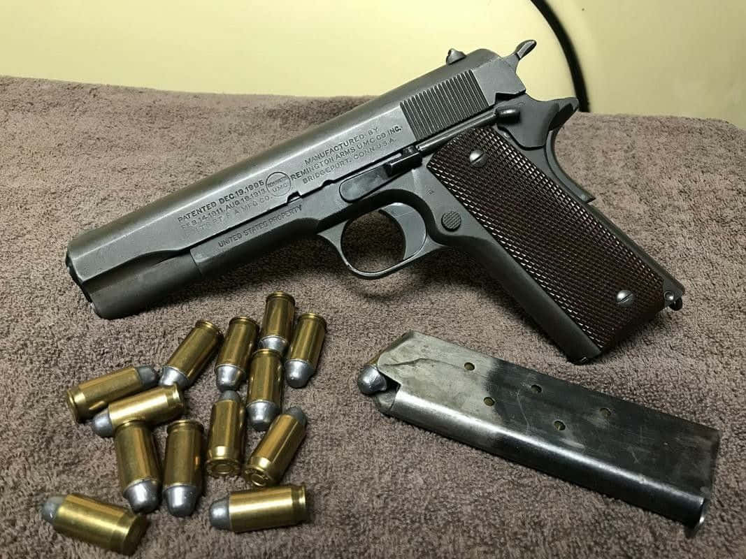 槍枝 桌布 壁紙 — 一把復古1911手槍，配有木製握把和黃銅子彈，放在棕色毛巾上，旁邊是其金屬彈匣。