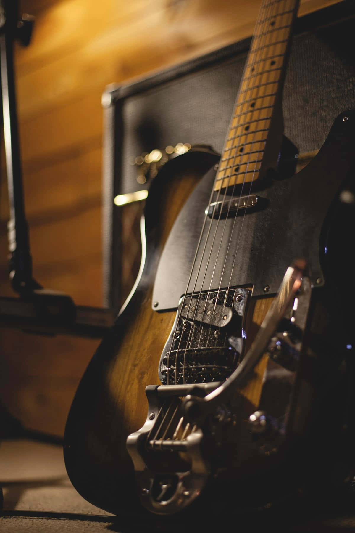 Guitar Aesthetic 桌布 壁紙 — 一把復古旭日紋電吉他放在溫暖燈光的木房間中，旁邊有一個揚聲器，背景柔和模糊。