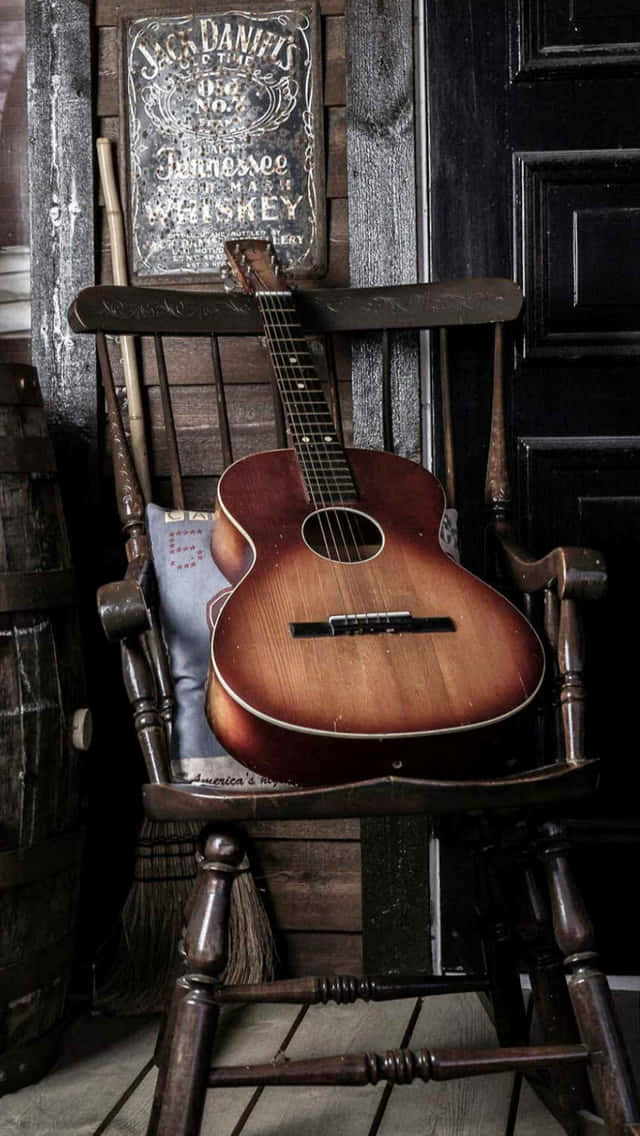 chair 桌布 壁紙 — 一把復古木吉他放在一張經風化的木搖椅上，旁邊有一個威士忌桶和一個Jack Daniel's標誌，位於一間鄉村小屋內。
