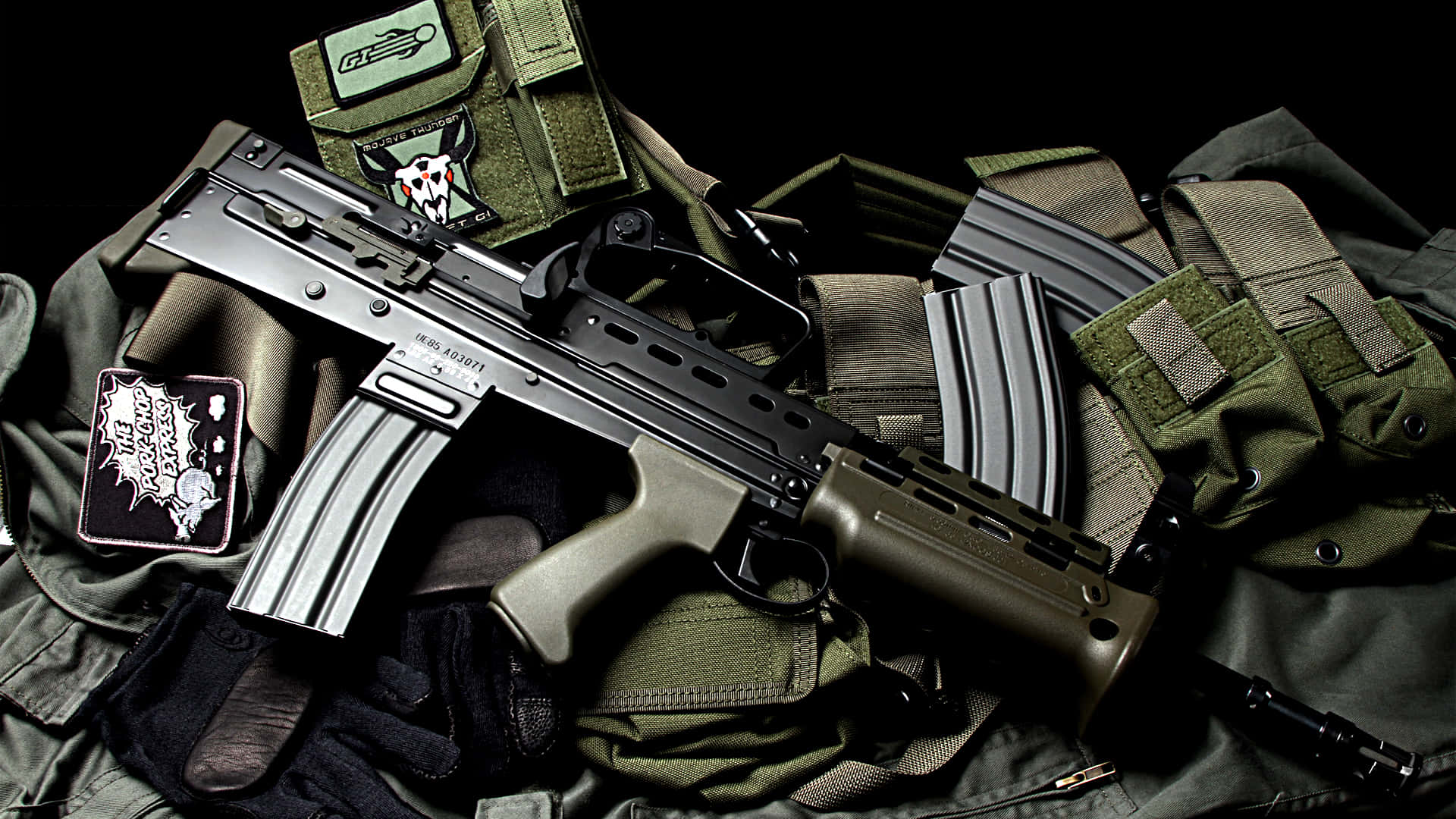 Rifle 桌布 壁紙 — 一把戰術步槍放在橄欖綠色的軍用裝備上，帶有徽章和彈匣，背景為黑色。