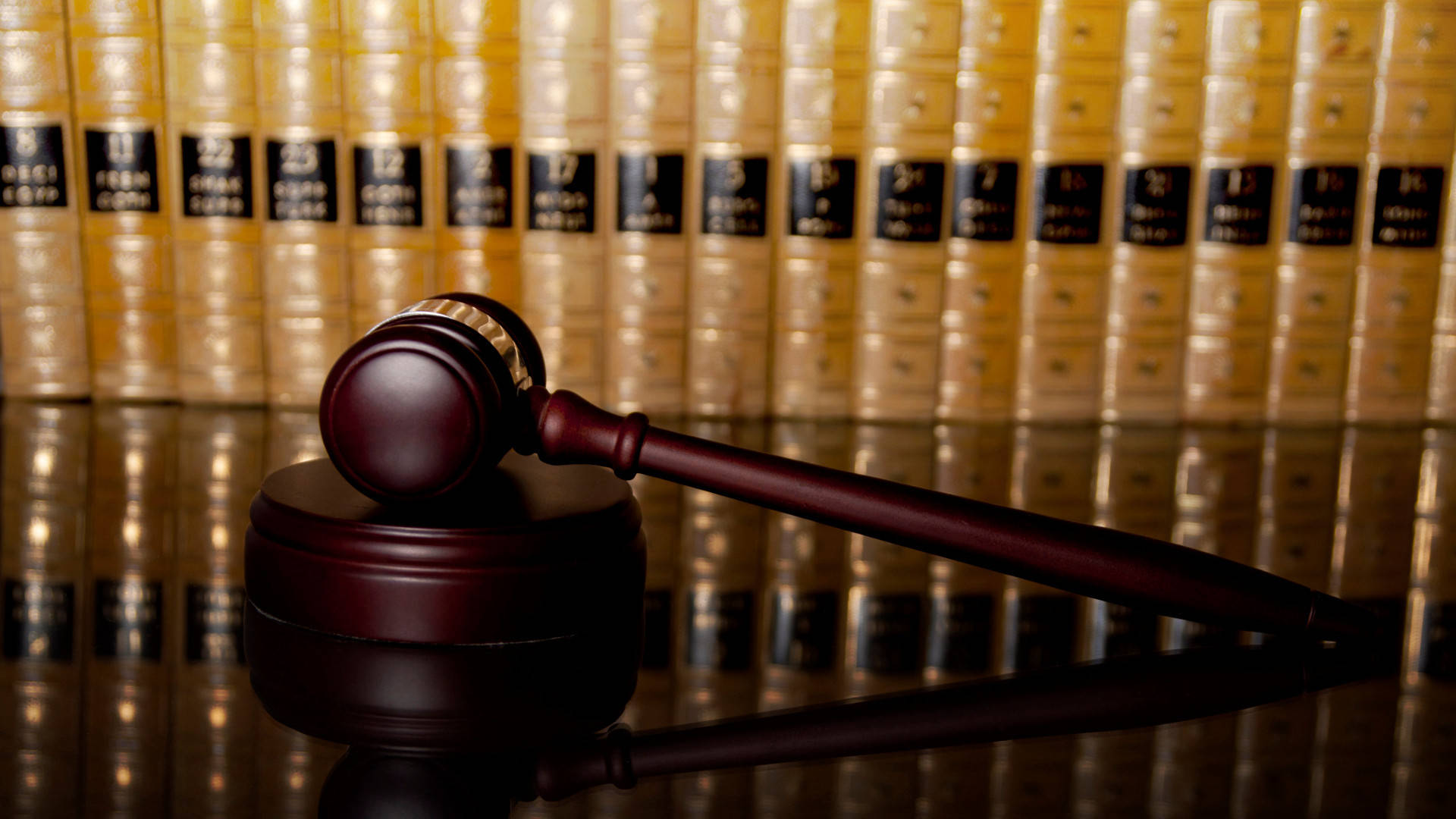 Lawyer 桌布 壁紙 — 一把拋光木槌放在其底座上，前面是一排金色法律書籍，在反射的法庭環境中。