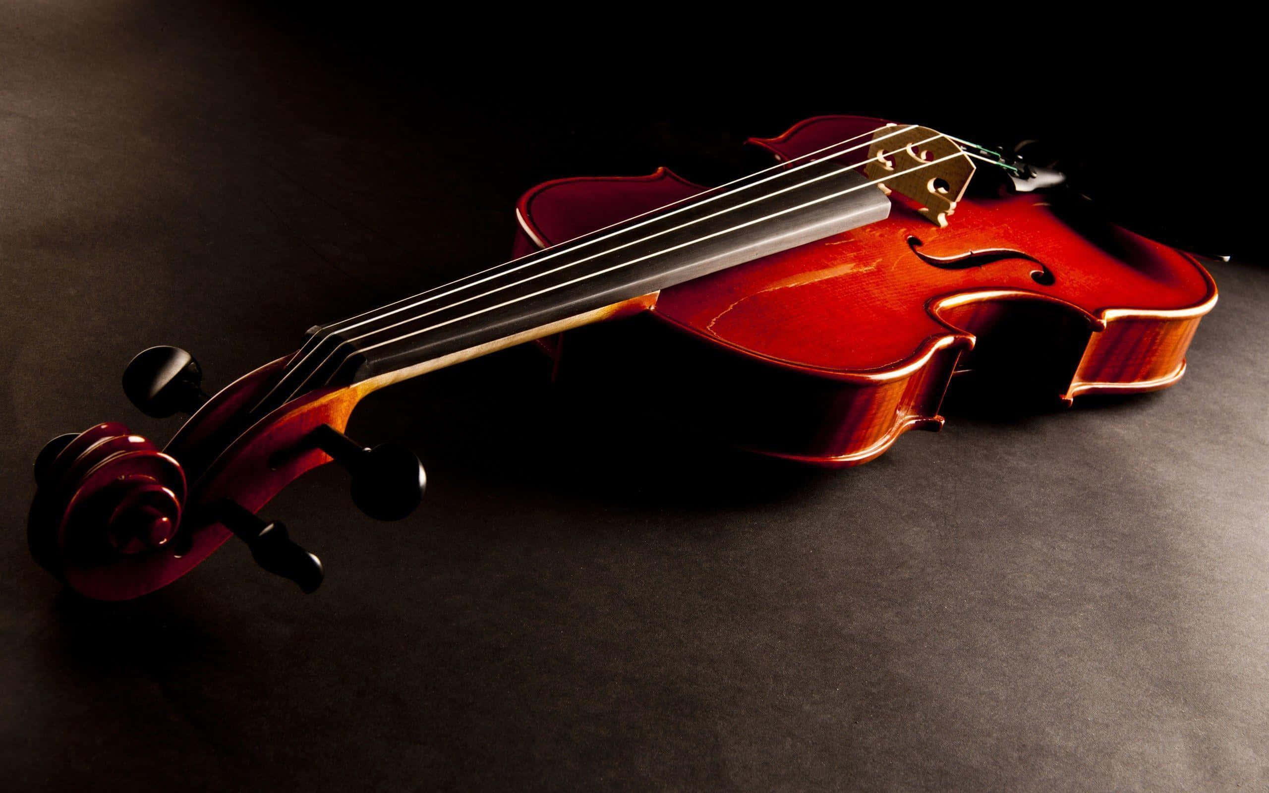 violin 桌布 壁紙 — 一把拋光精美的小提琴斜放在深色表面上，戲劇性的燈光突顯其曲線和木紋。