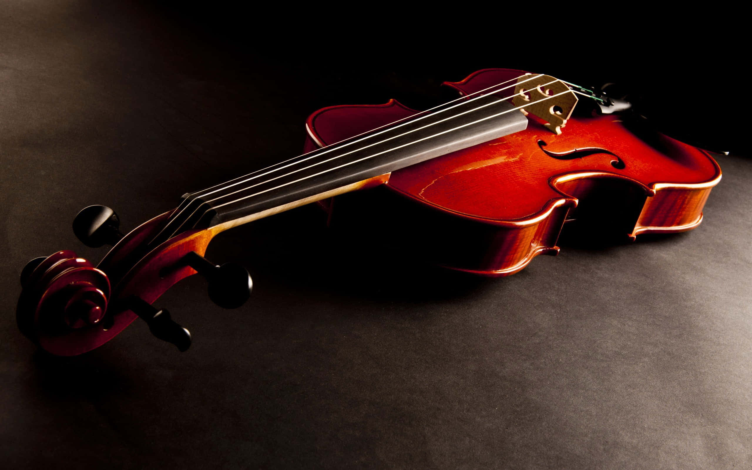 violin 桌布 壁紙 — 一把拋光精良的小提琴斜放在深色紋理表面上，戲劇性的燈光突顯其曲線和木紋。