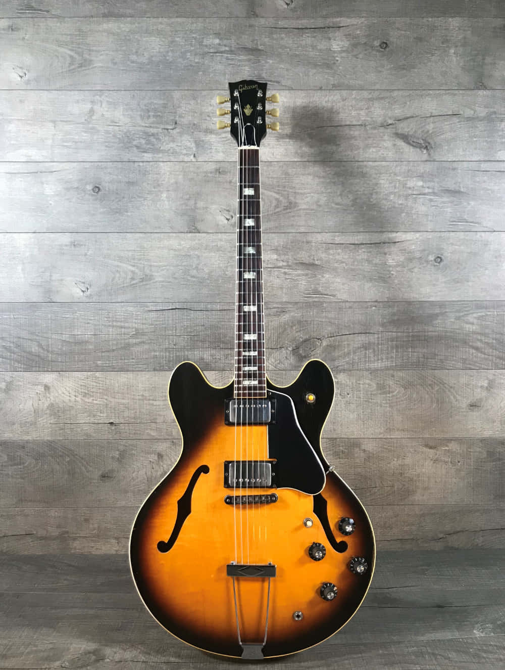 Guitar Aesthetic 桌布 壁紙 — 一把旭日色Gibson ES-335電吉他，配有黑色護板及金色硬件，垂直靠在一面風化灰色的木牆上。