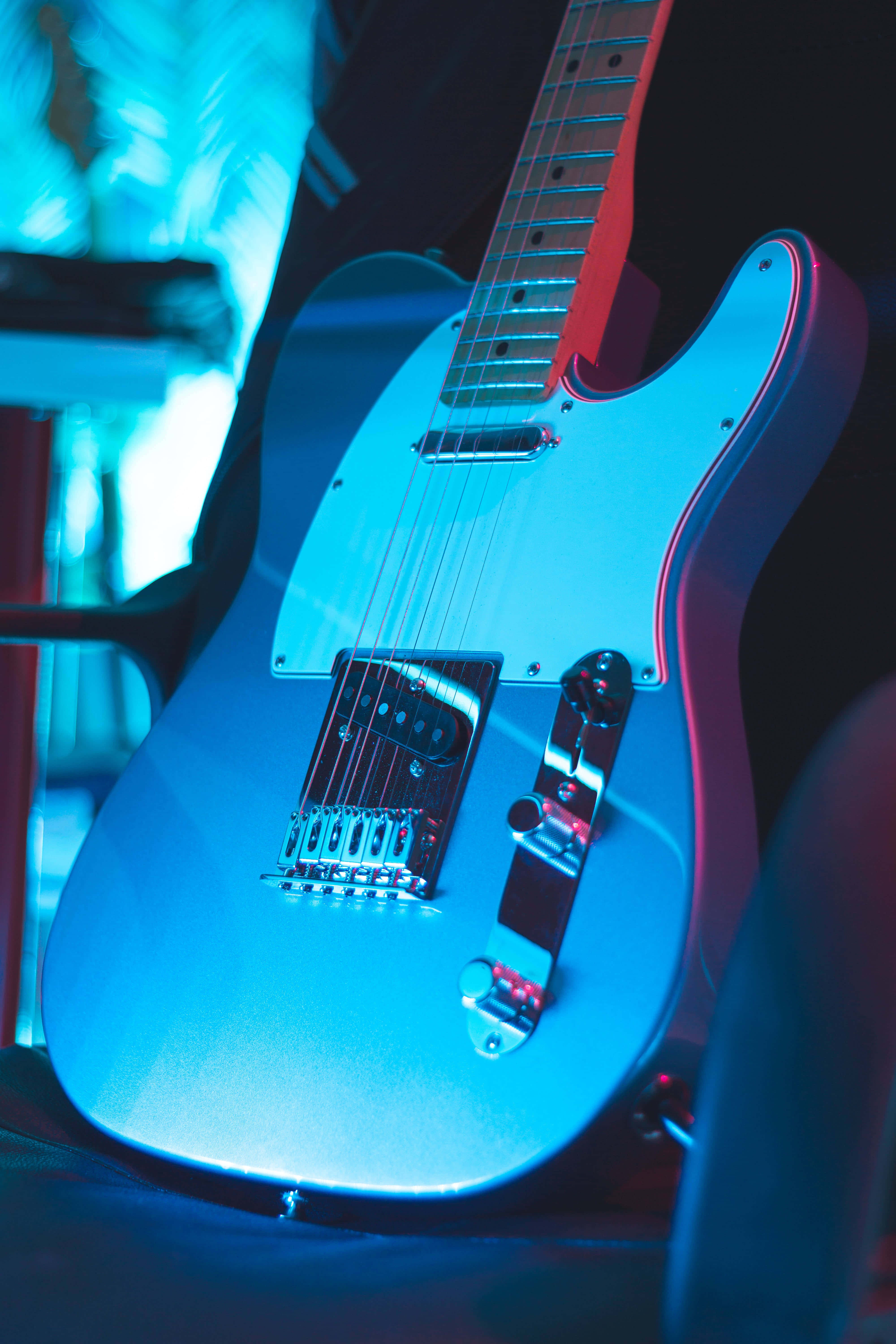 Guitar Aesthetic 桌布 壁紙 — 一把時尚的藍色電吉他在充滿活力的舞台燈光下閃耀，琴身和琴頸帶有紅色點綴。