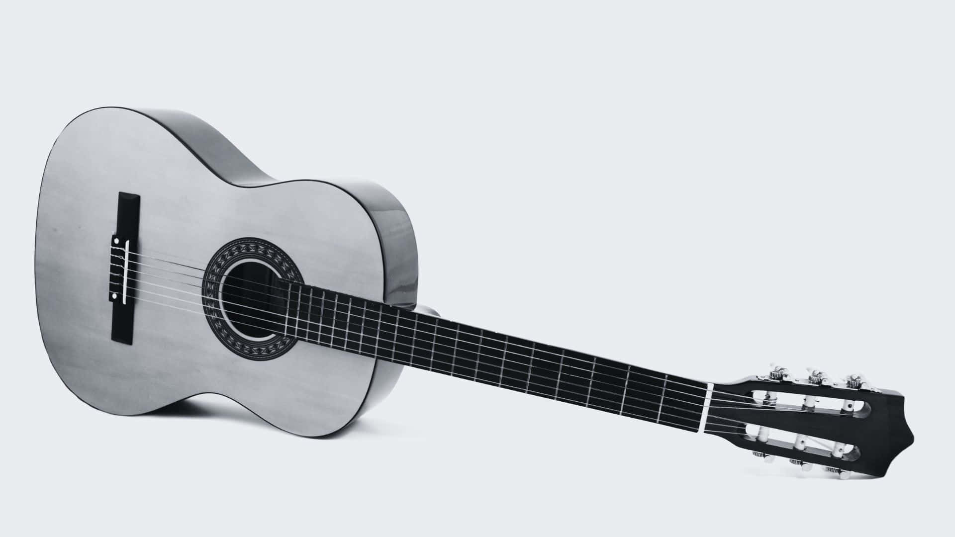 Black And White Guitar 桌布 壁紙 — 一把時尚的銀色古典吉他斜靠在柔和的灰色背景上，展現其優雅的曲線和深色指板。