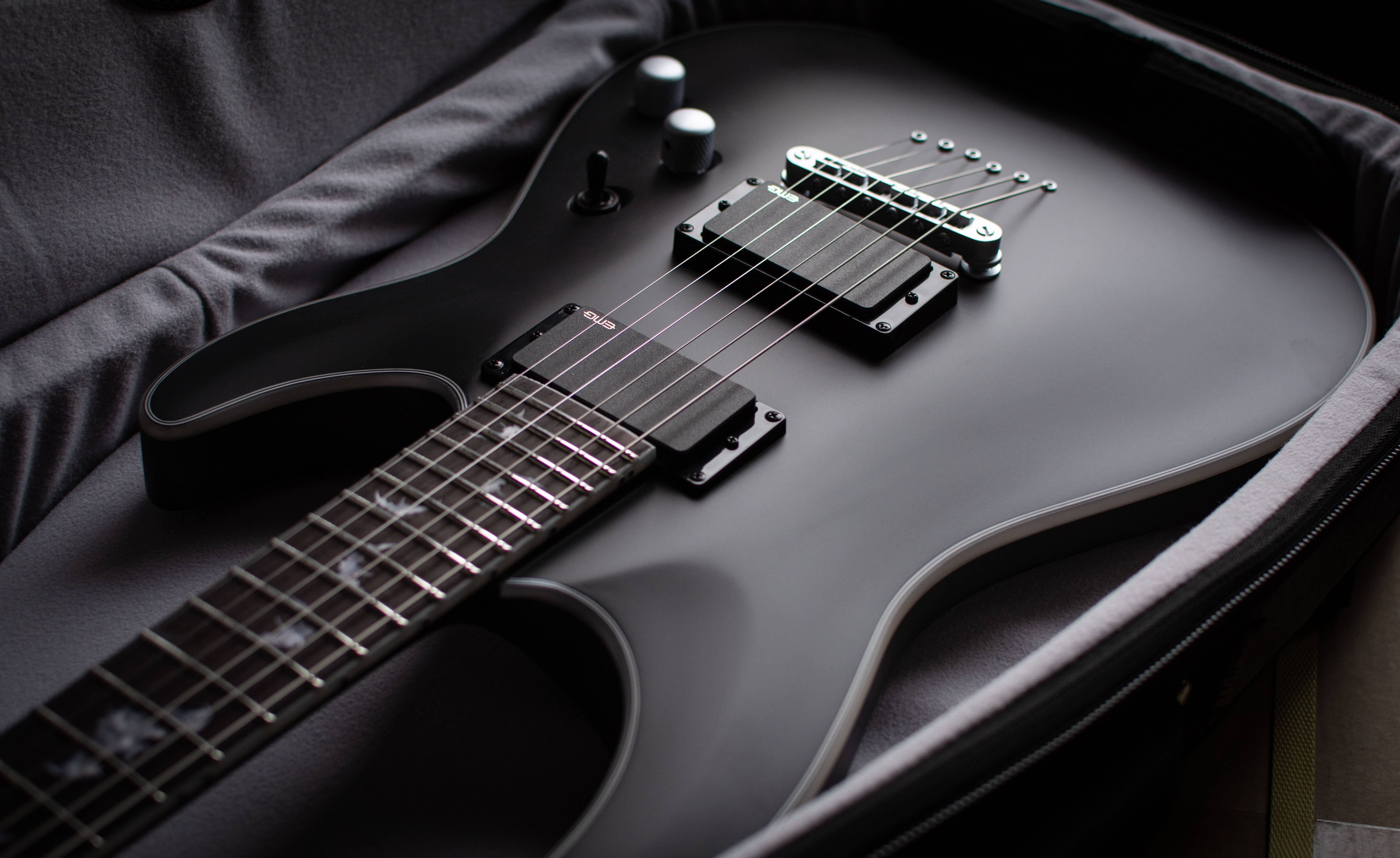 Guitar Aesthetic 桌布 壁紙 — 一把時尚的霧面黑色電吉他放置在軟墊箱內，柔和燈光突顯其曲線和金屬硬件。