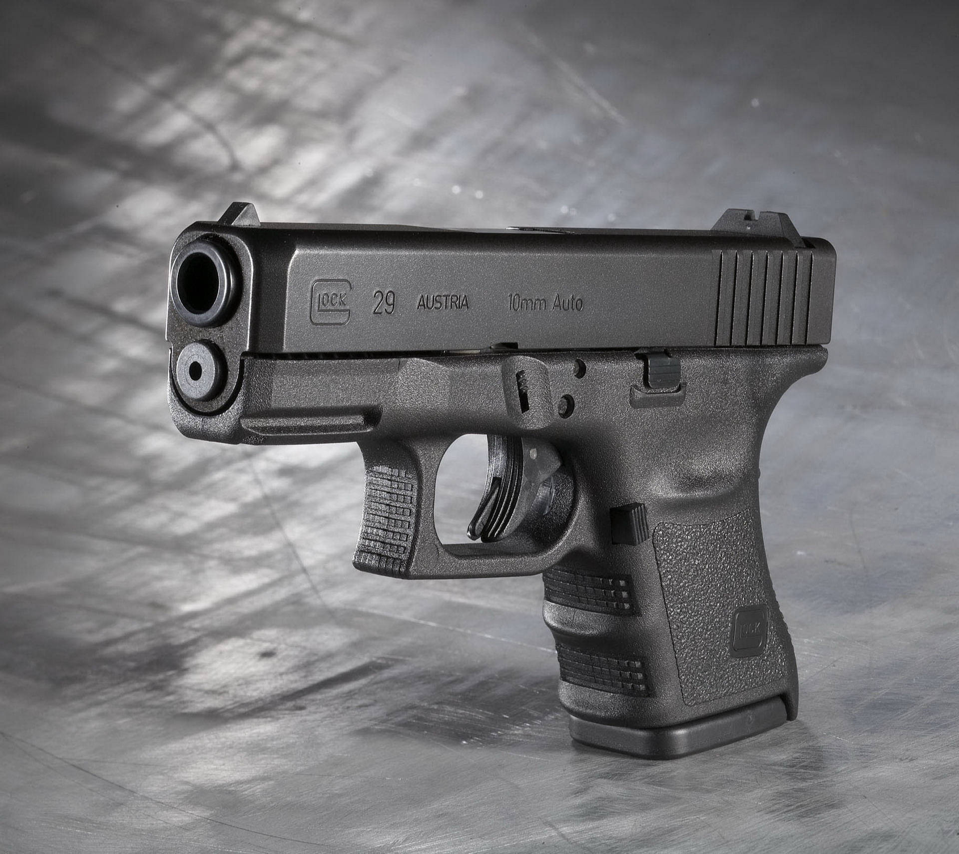 克拉克 桌布 壁紙 — 一把時尚的黑色 Glock 29 手槍放在有紋理的金屬表面上，在戲劇性的工作室燈光下。
