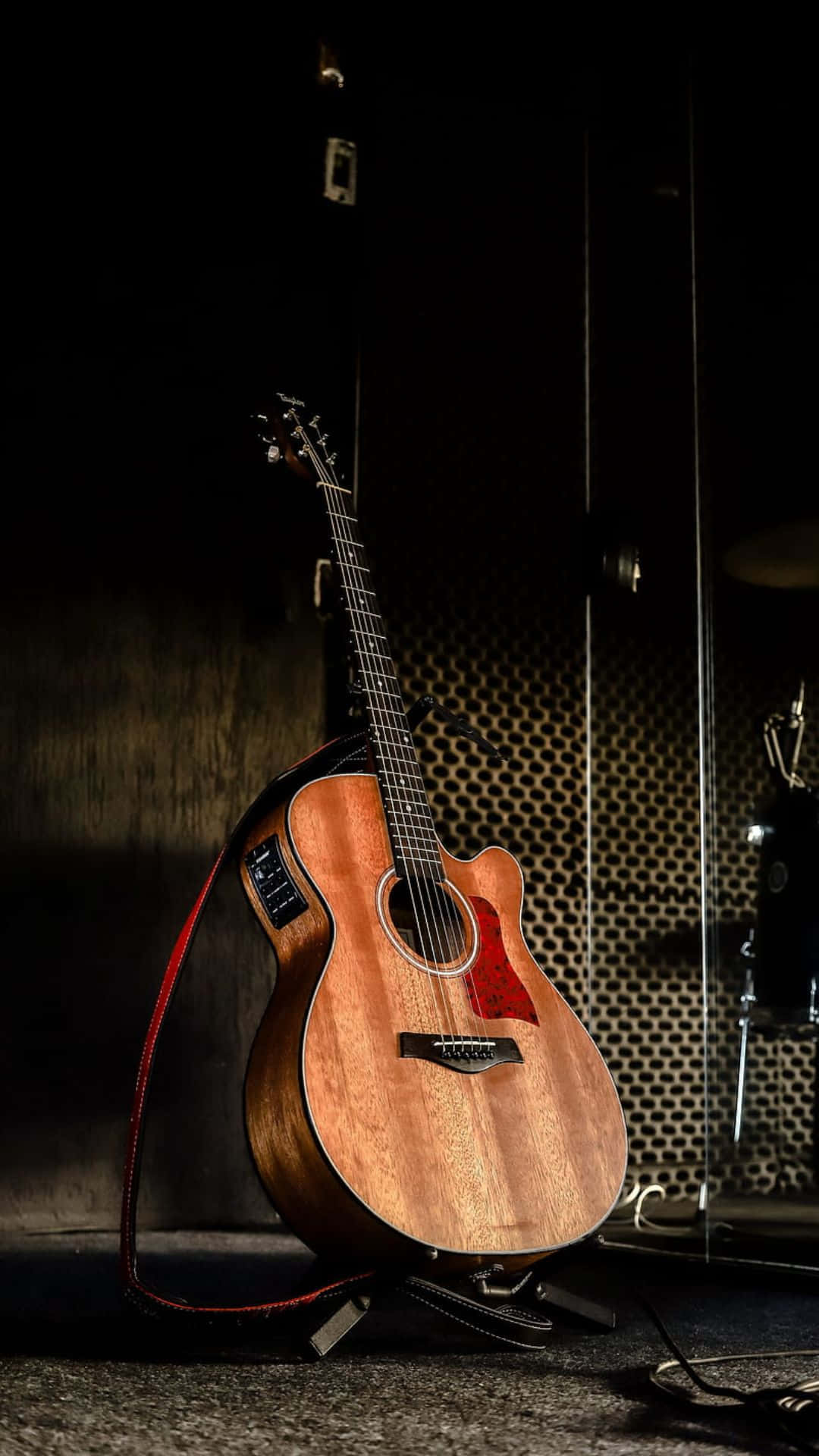 Guitar Aesthetic 桌布 壁紙 — 一把暖色調的吉他帶有紅色邊飾，直立於支架上，背景為深色穿孔金屬。