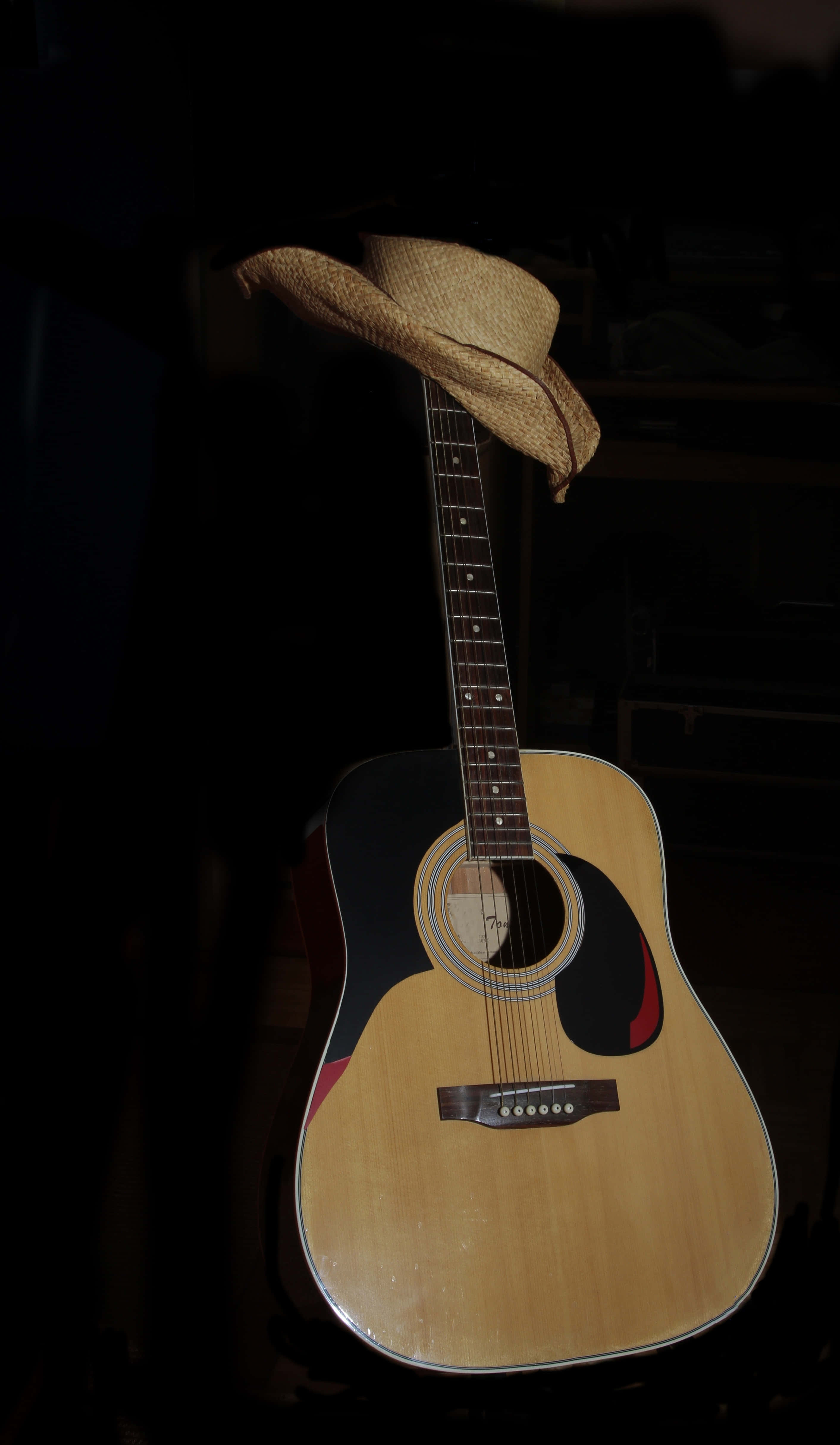 Guitar Aesthetic 桌布 壁紙 — 一把木製原聲吉他，其琴頸上放著一頂草帽，在柔和光線下襯托著深色背景。