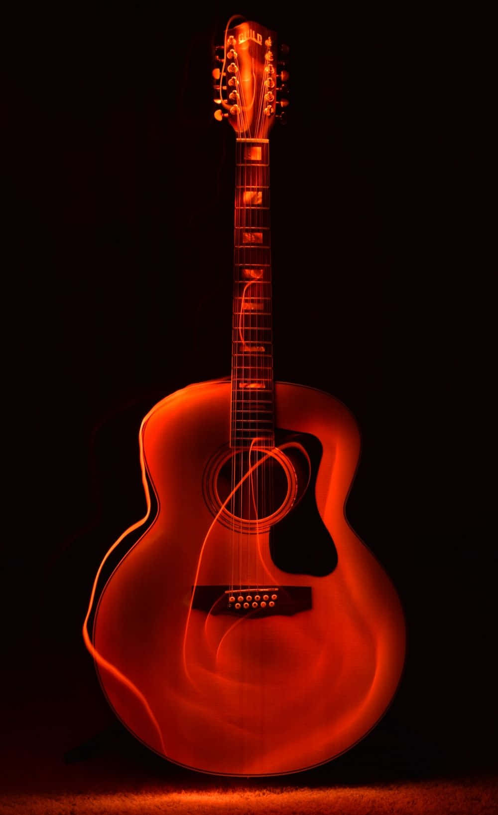 Musical 桌布 壁紙 — 一把溫暖照明的原聲吉他在漆黑背景中散發著豐富的琥珀色調，柔和的光跡在其琴身周圍盤旋。
