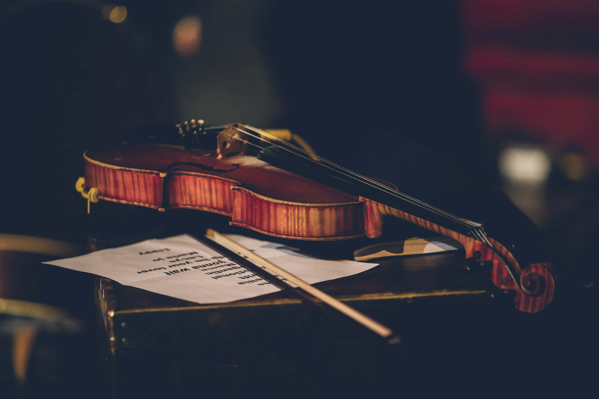 violin 桌布 壁紙 — 一把溫暖燈光照耀的小提琴優雅地擱在樂譜上，置於一個光線昏暗的音樂廳的木製譜架上。