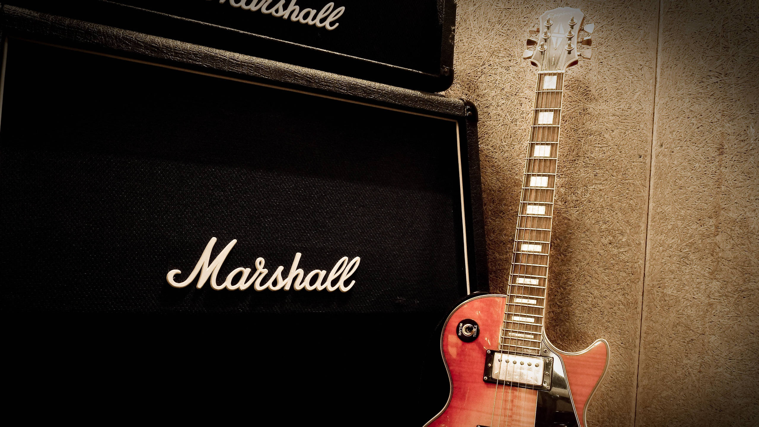 Marshall 桌布 壁紙 — 一把漸層色電吉他靠在一面有紋理的牆上，旁邊有兩個帶發光標誌的黑色Marshall擴音器。