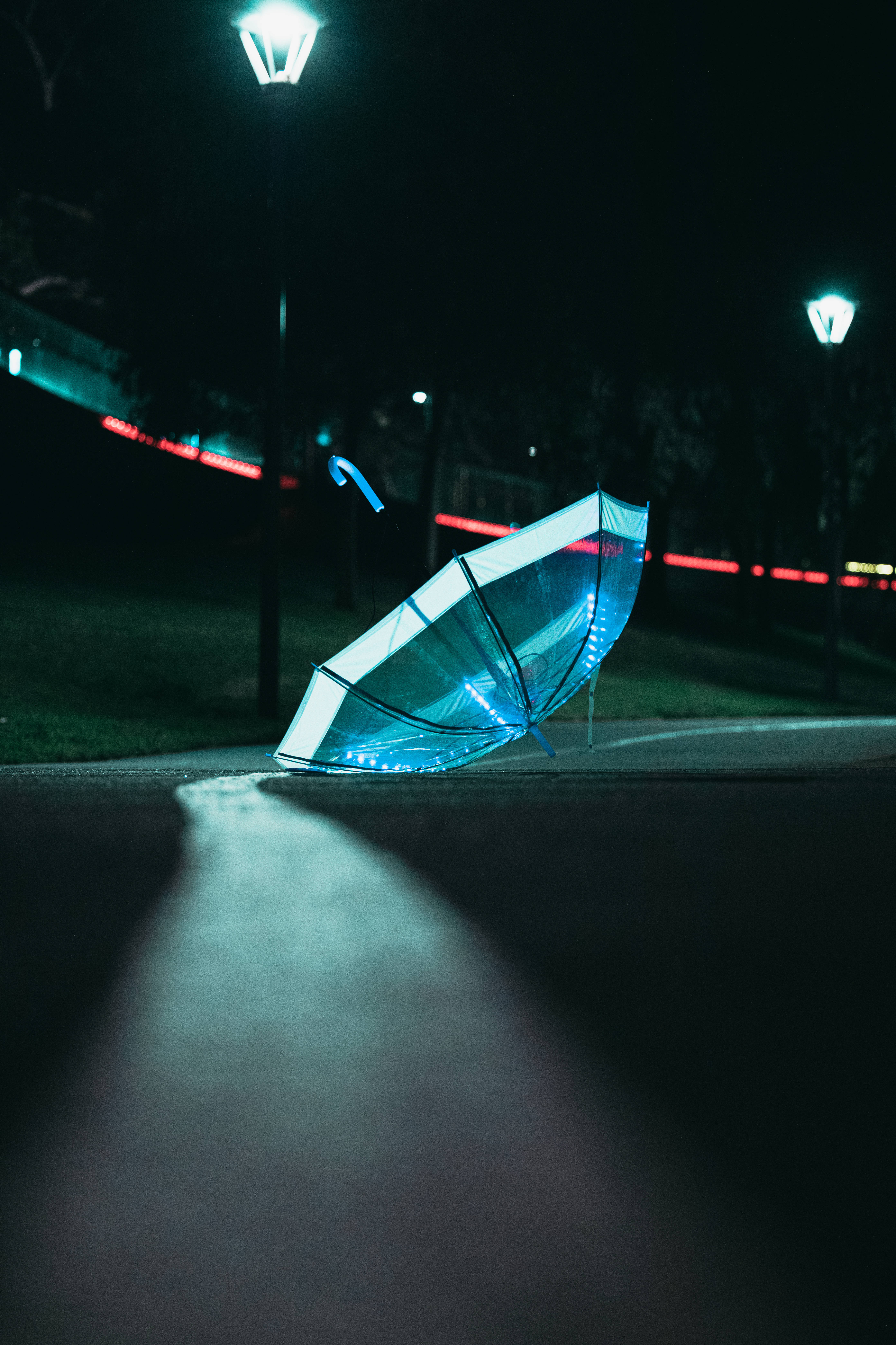 lights 桌布 壁紙 — 一把發光的藍色透明雨傘放在夜晚街燈下的濕漉漉人行道上，背景有紅色光跡。