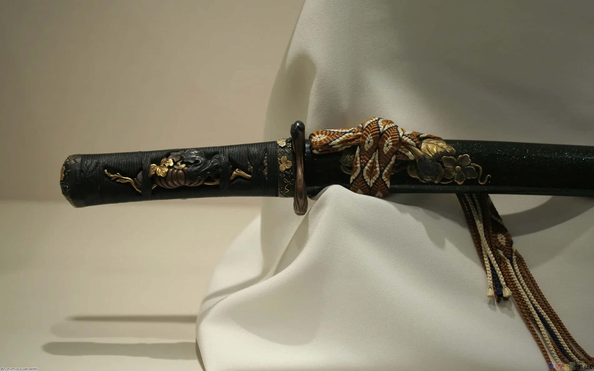 Samurai Sword 桌布 壁紙 — 一把精緻的日本刀，帶有金色花卉鑲嵌，優雅地放置在白色布料上，背景為中性色調。