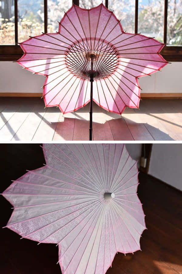 Umbrella 桌布 壁紙 — 一把精緻的粉紅色櫻花傘在室內打開，在木地板上投下柔和陰影，第二個視角展示其半透明面板和精緻框架。