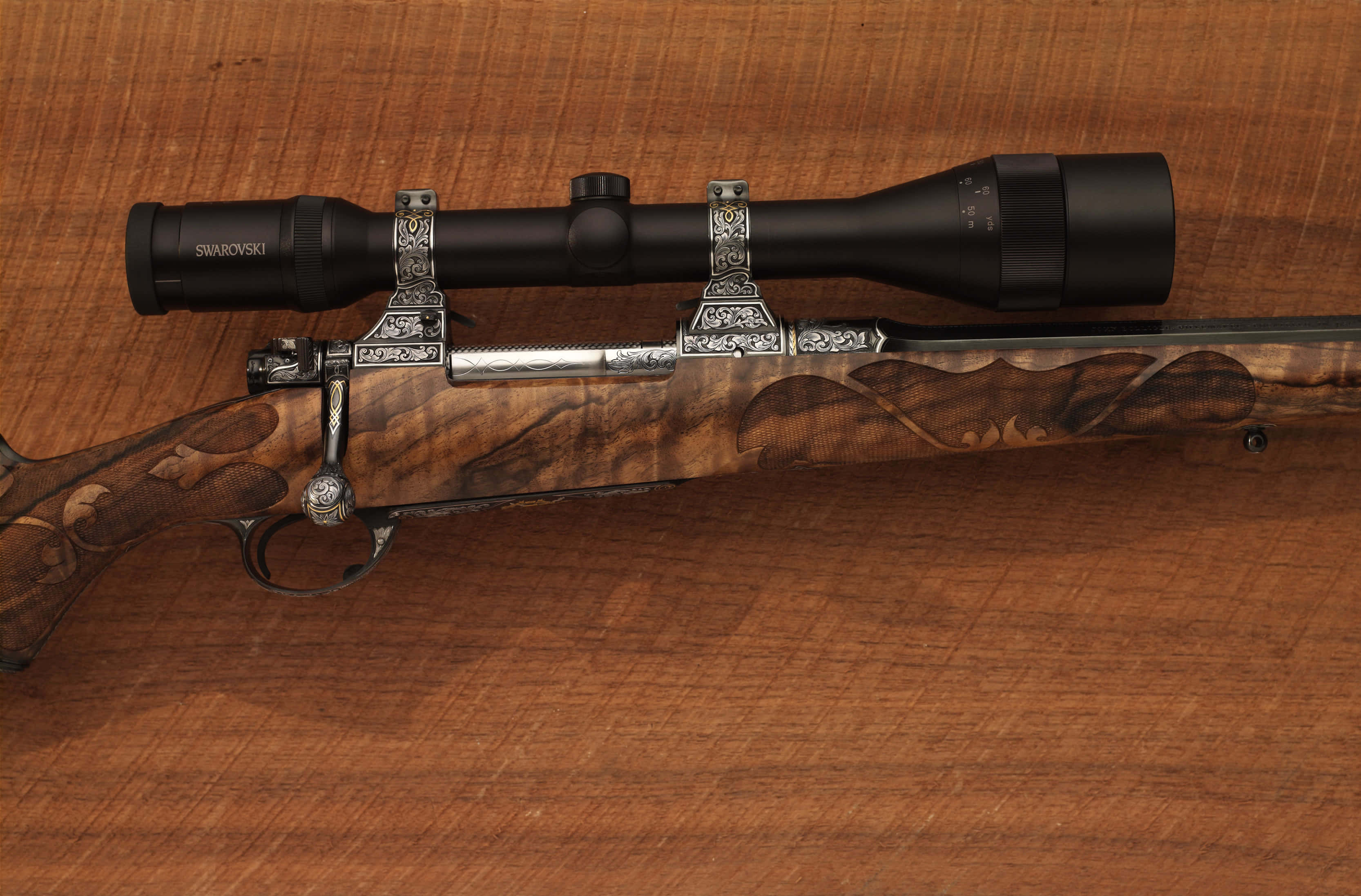 Rifle 桌布 壁紙 — 一把精緻製作的步槍，帶有華麗的銀色細節和施華洛世奇瞄準鏡，放置在華麗的木質表面上。