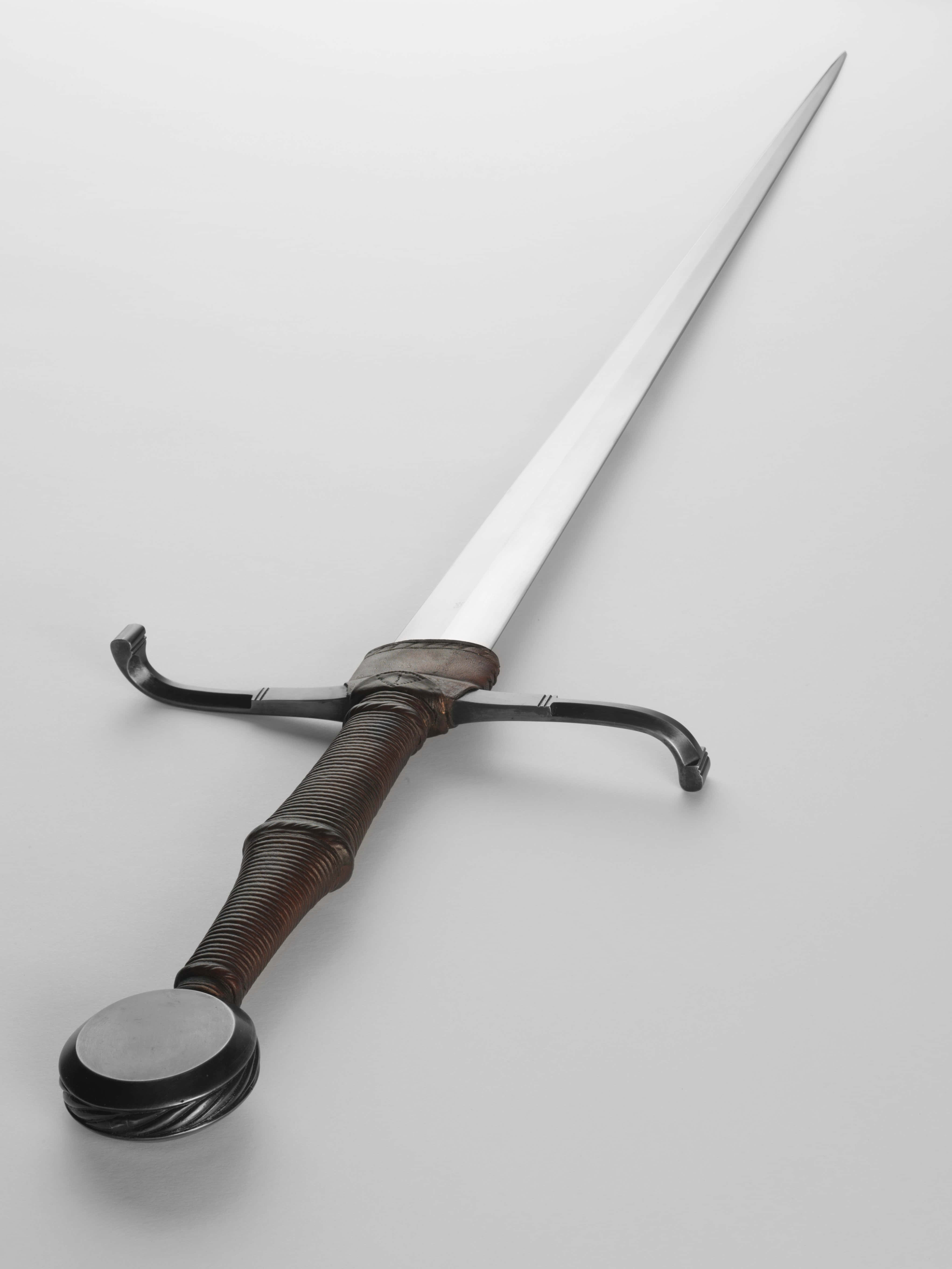 Ancient Weapons 桌布 壁紙 — 一把細節豐富的中世紀劍，帶有扭曲握柄和彎曲護手，斜放在純白表面上。