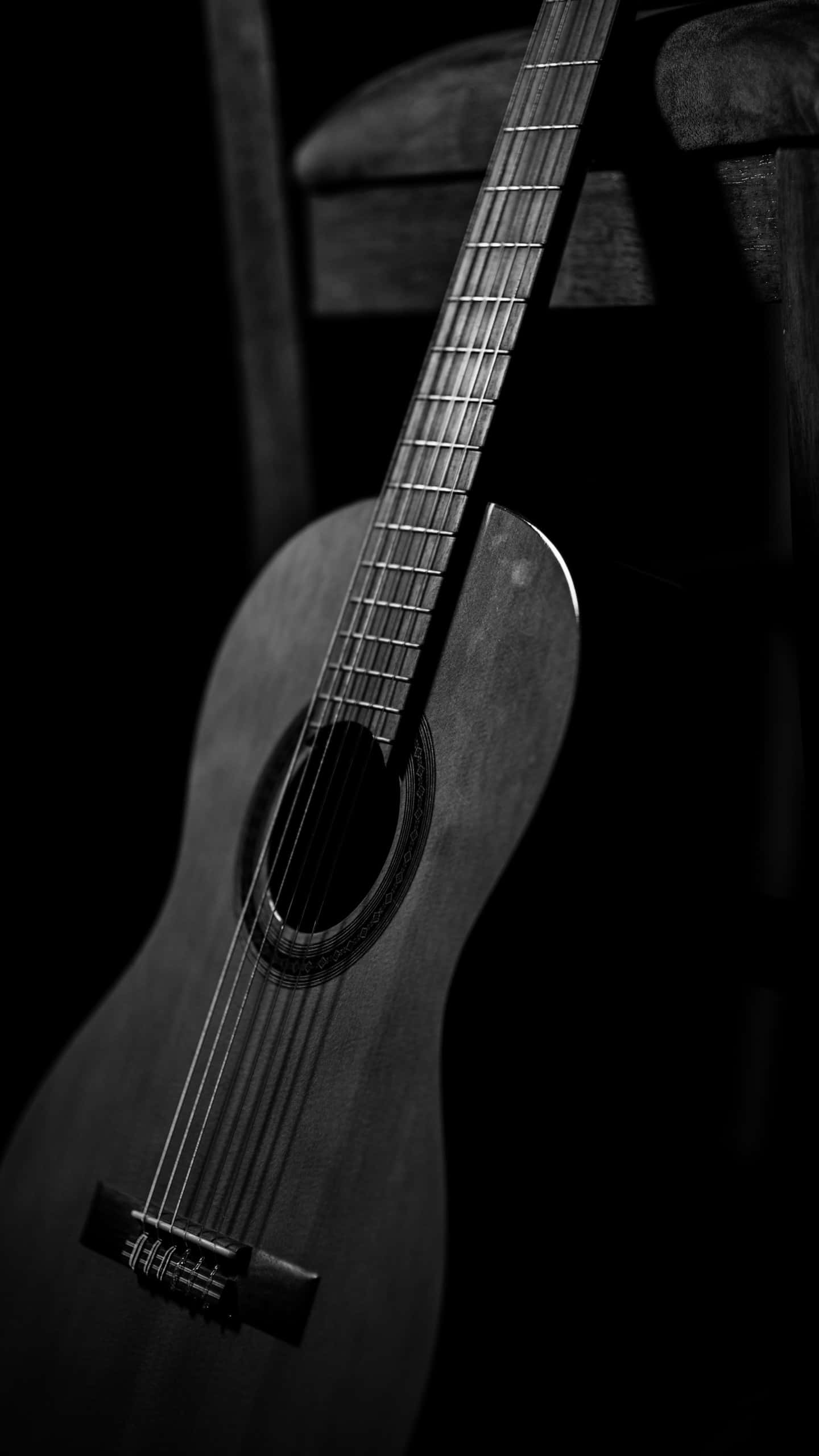 Acoustic Guitar 桌布 壁紙 — 一把經典原聲吉他在陰影中靜止地靠在木椅上，構成單色畫面。