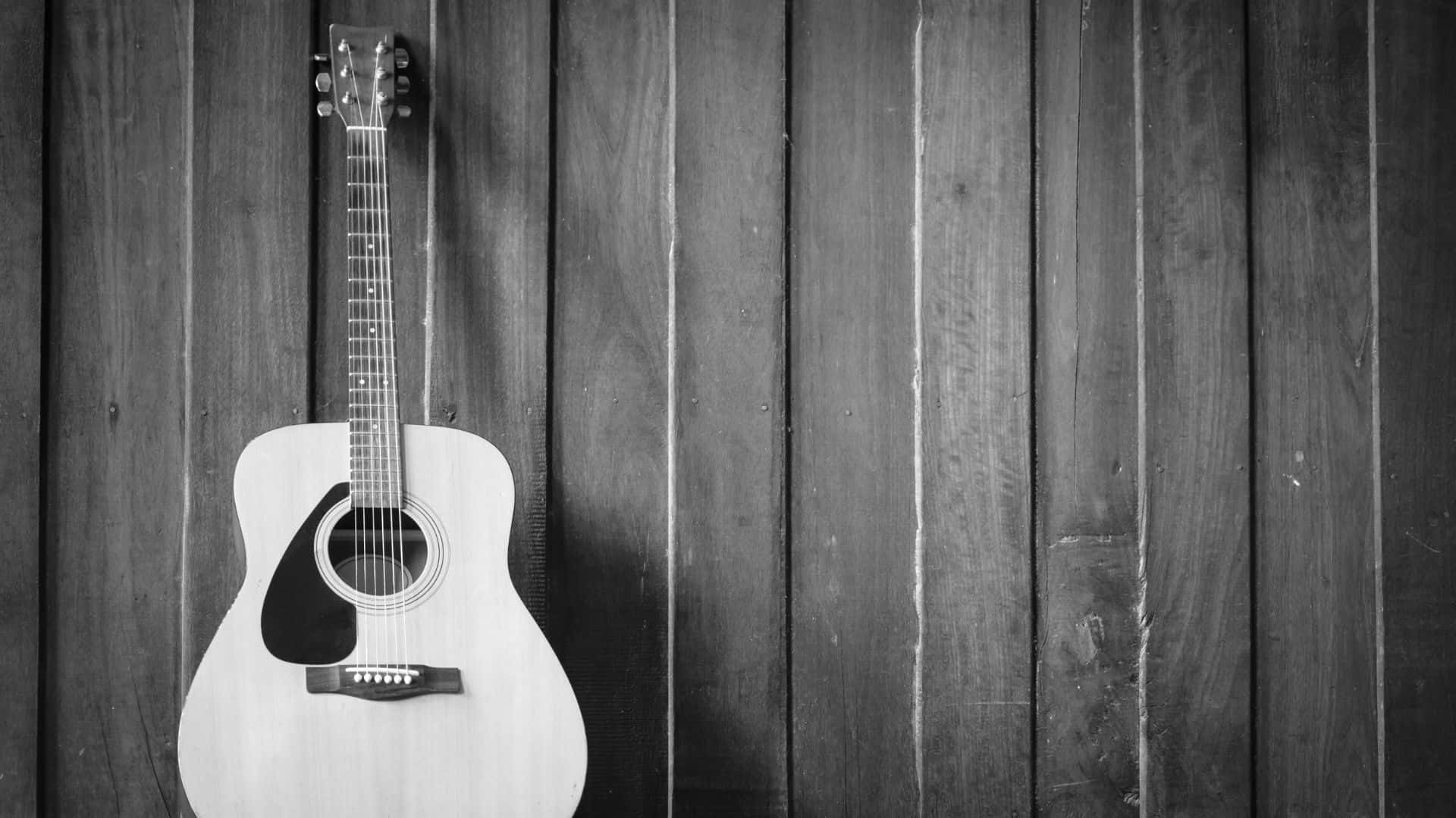 Black And White Guitar 桌布 壁紙 — 一把經典木吉他掛在風化的木牆上，以黑白呈現，喚起質樸的音樂懷舊感。
