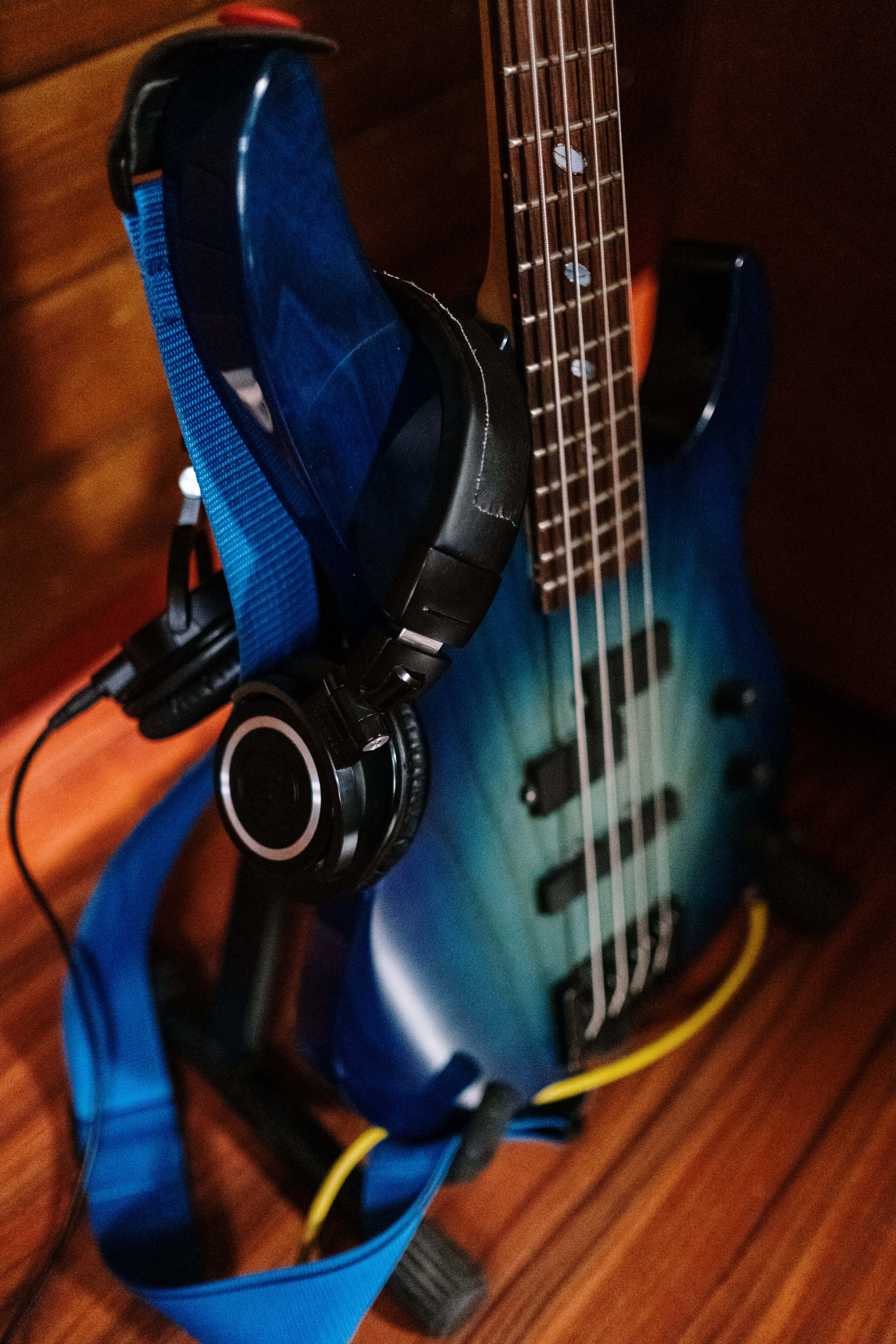 Bass Guitar 桌布 壁紙 — 一把藍色漸層低音吉他，黑色耳機掛在琴頸上，放在木地板上。