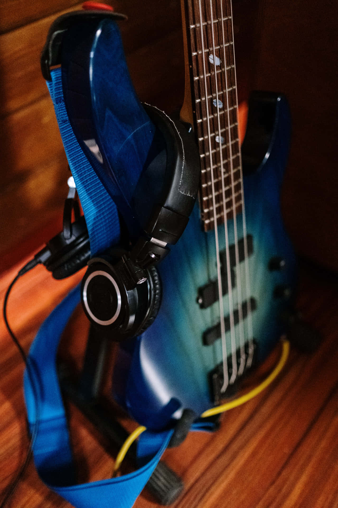 Guitar Aesthetic 桌布 壁紙 — 一把藍色漸變低音吉他，黑色耳機掛在琴頸上，放在木地板上。