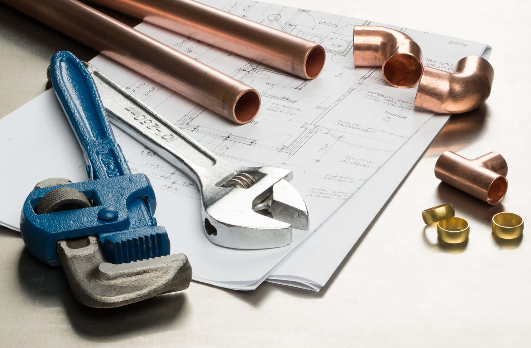 Plumbing 桌布 壁紙 — 一把藍色管鉗和銀色可調扳手放在藍圖上，銅管和配件整齊地排列在金屬表面上。