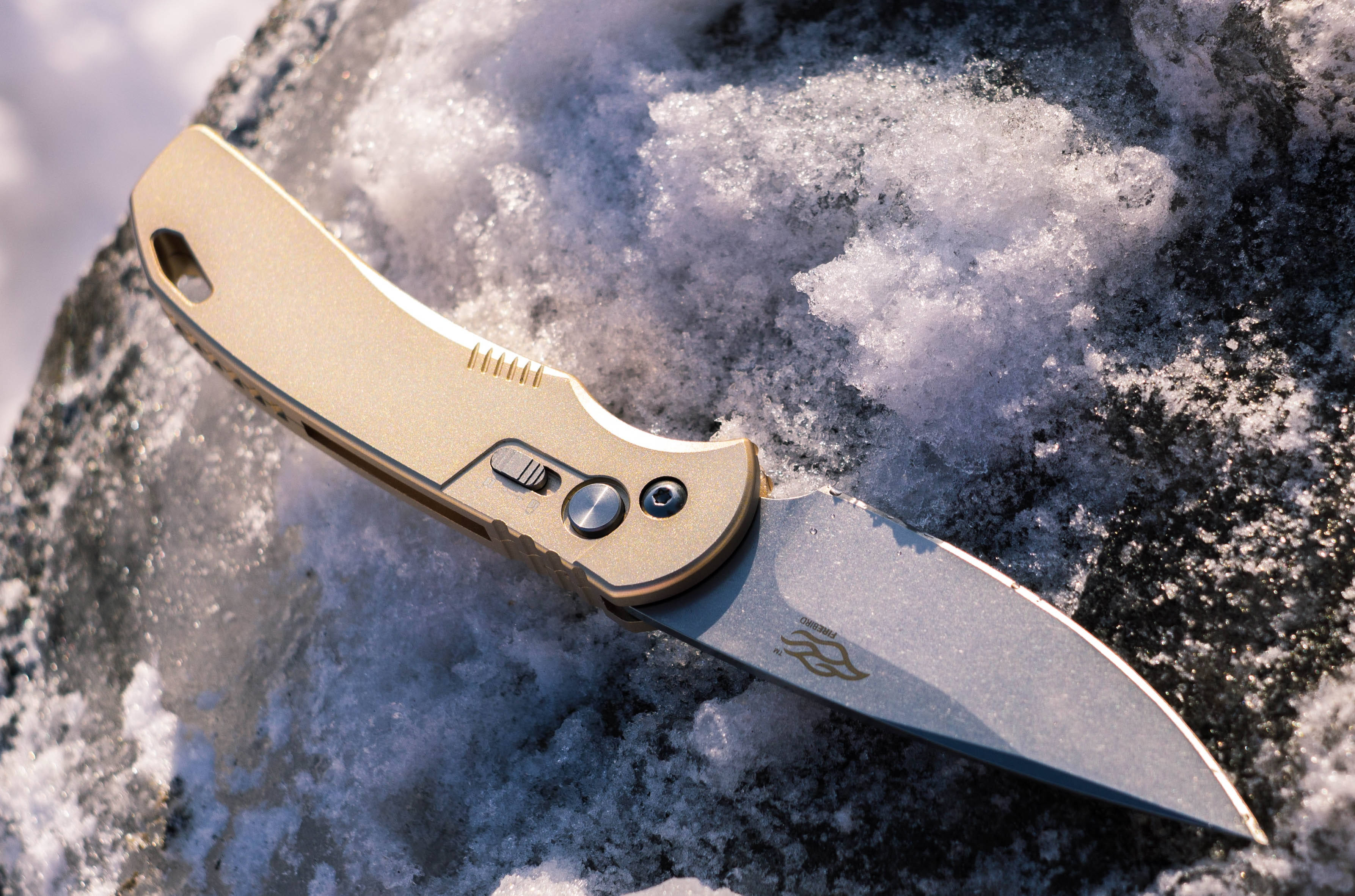 Danger 桌布 壁紙 — 一把金色折疊刀放在陽光普照的雪石上。